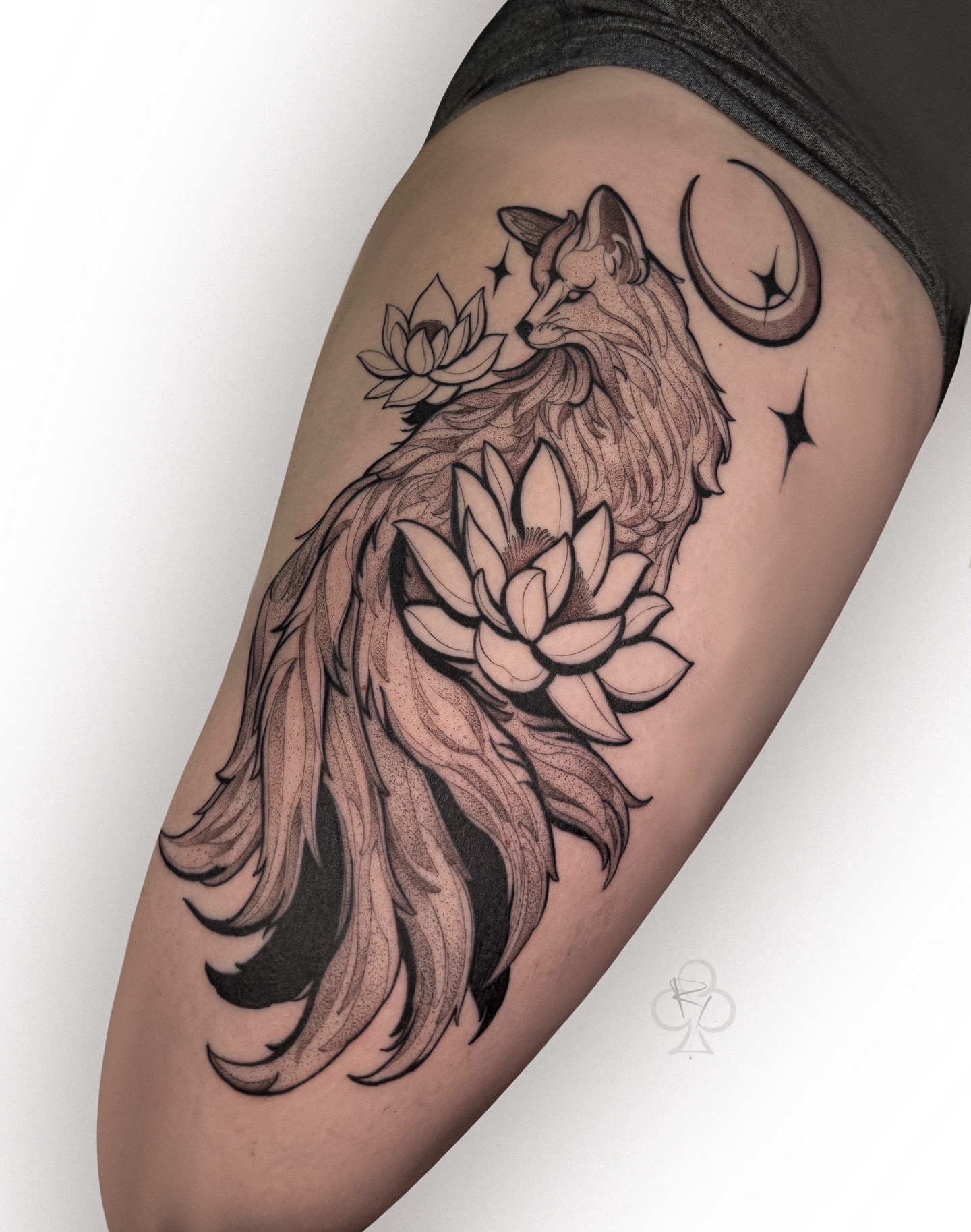 Tattoo of a wolf with a flowing mane, lotus flowers, a crescent moon, and stars on a person's thigh.
