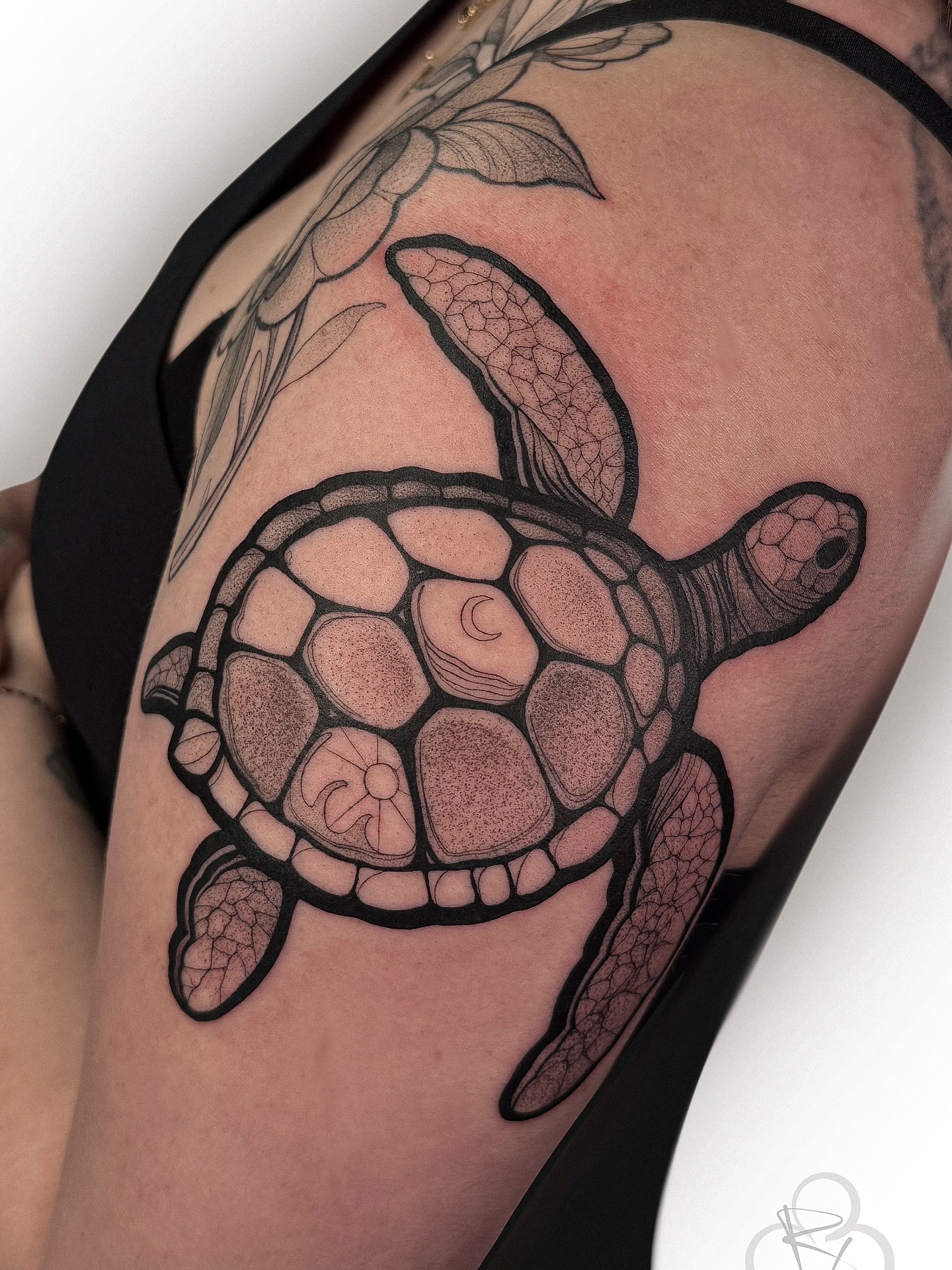 Turtle tattoo with detailed shell and flippers on person's upper arm, with additional floral design nearby.