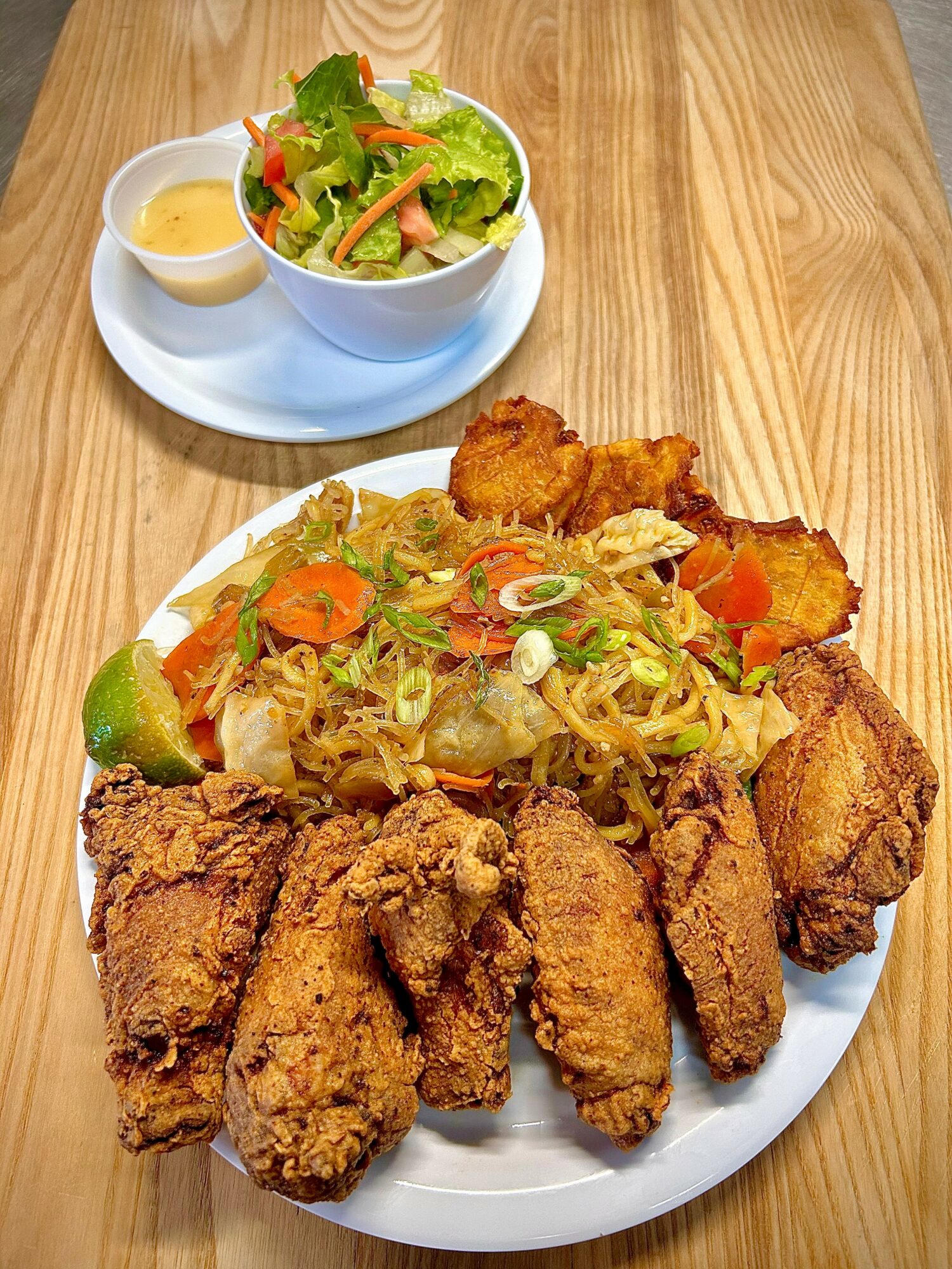 Plate with fried chicken pieces, noodle salad with vegetables, and a side of lime, with a salad in a bowl behind.