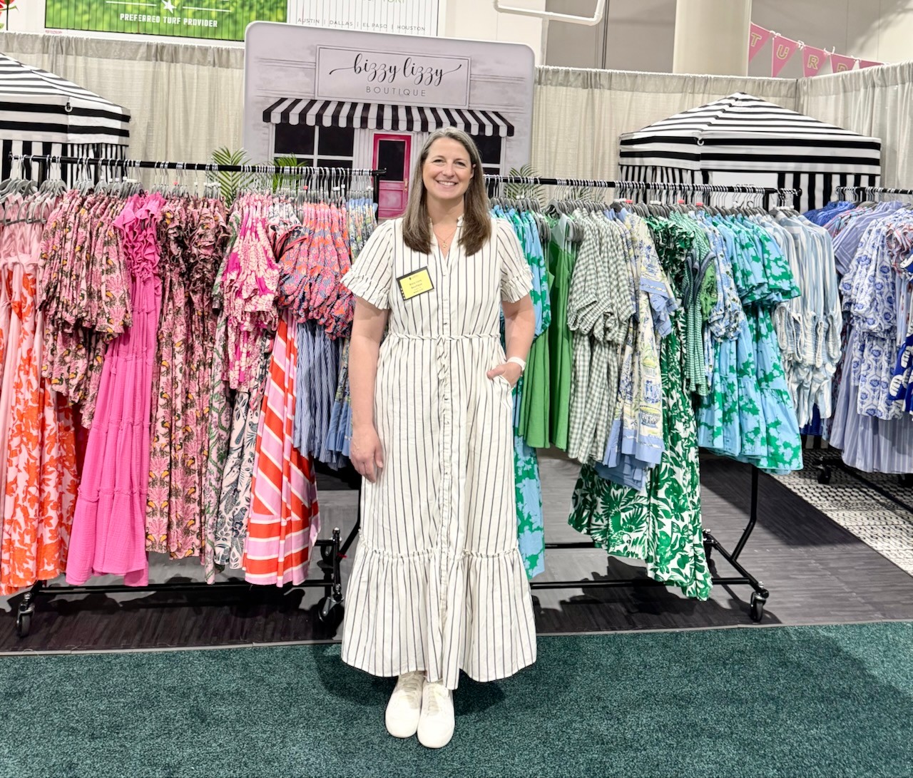Woman in a striped dress standing in front of colorful dresses on racks inside a store.