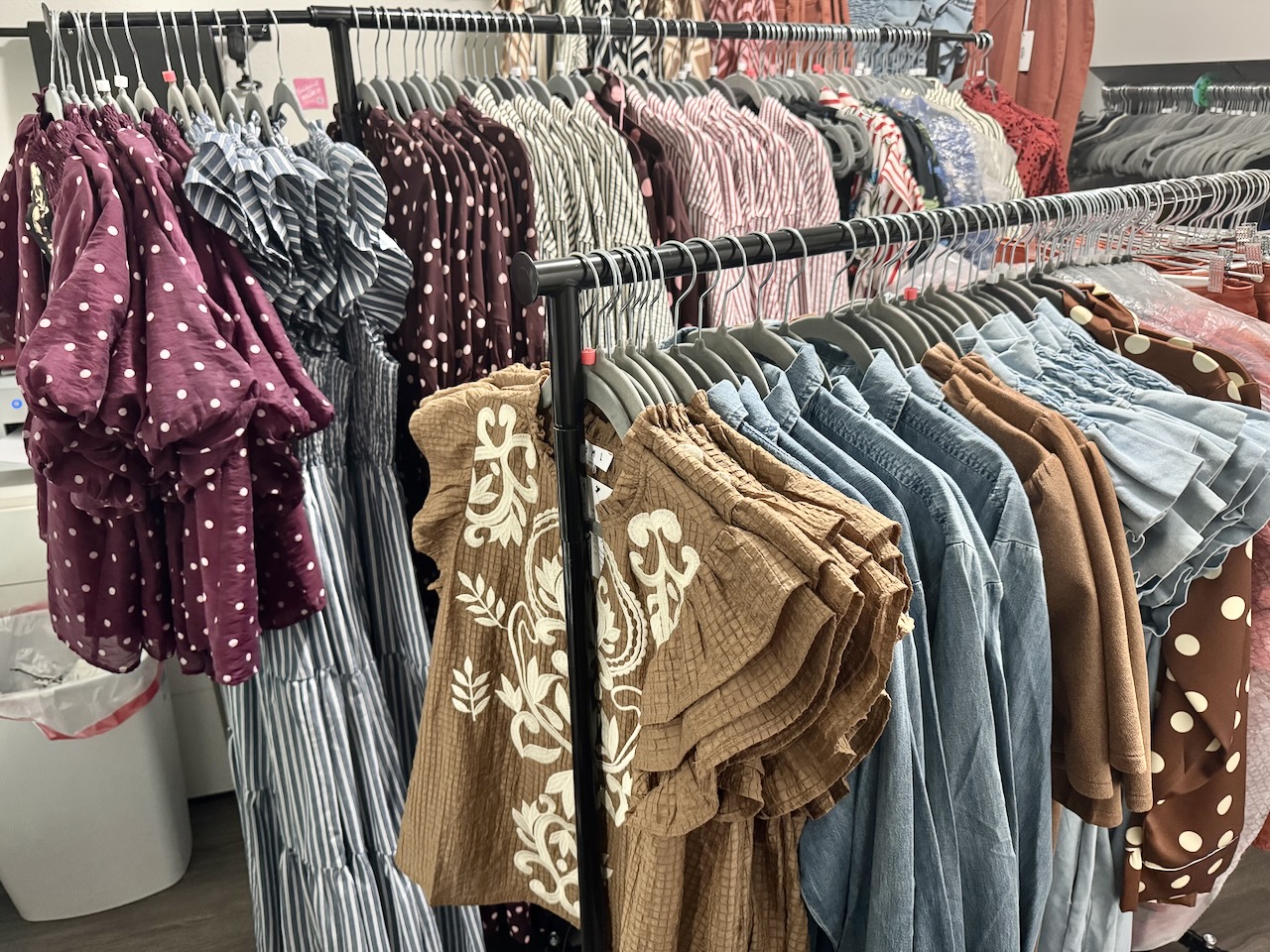 Clothing rack with various dresses and shirts in different colors and patterns, including polka dots and floral designs.