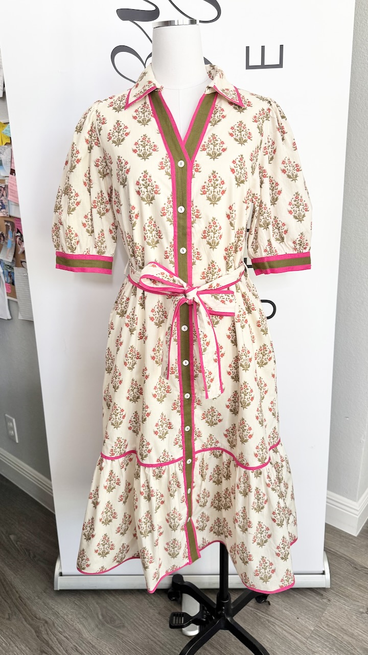 Long floral dress with pink trim and a waist tie displayed on a mannequin, against a white background.