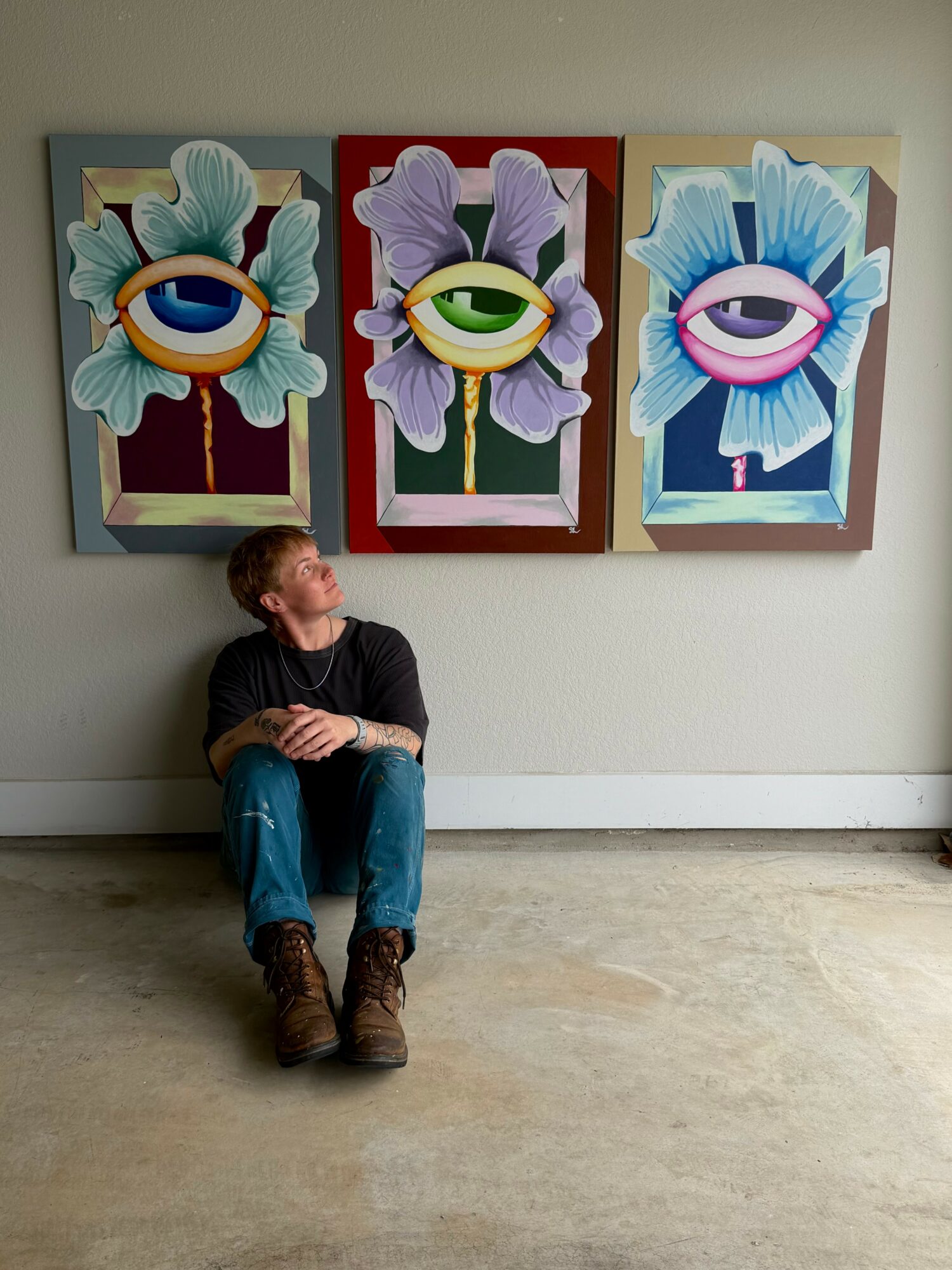 Child sitting on the floor looking at three colorful floral eye paintings on the wall.