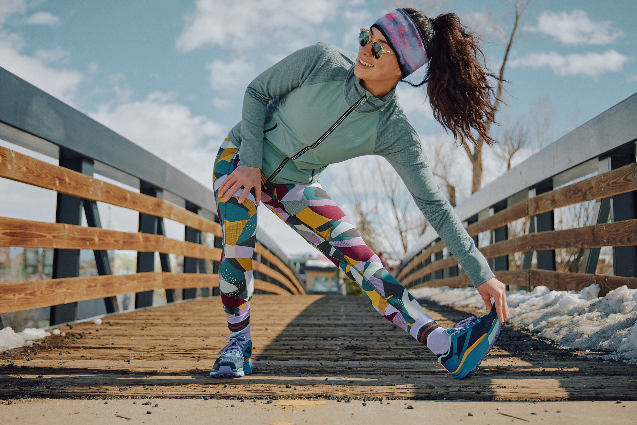 Person stretching on a wooden bridge, wearing colorful leggings and a headband.