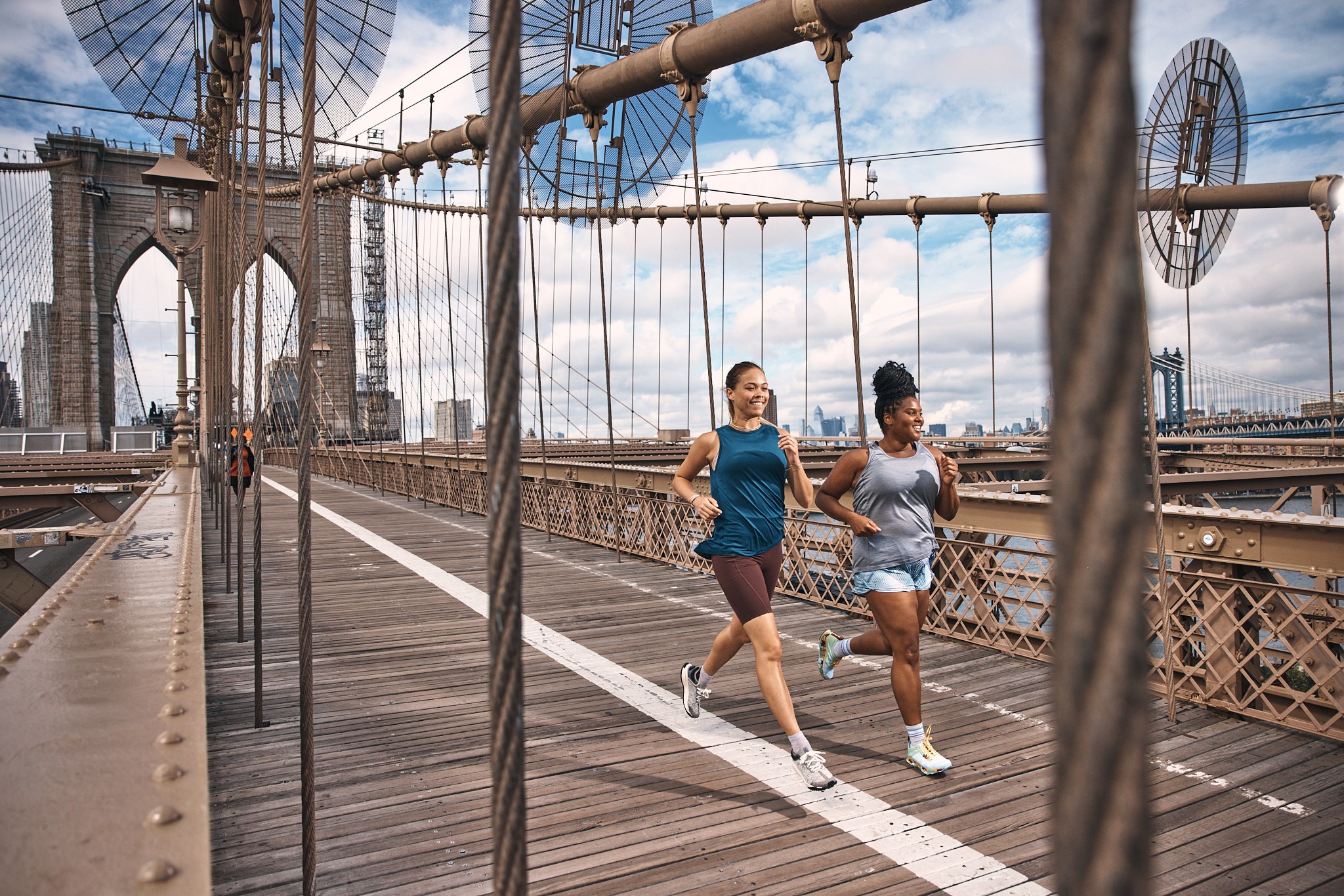 Two people jogging across a suspension bridge, with cables and a stone tower visible.