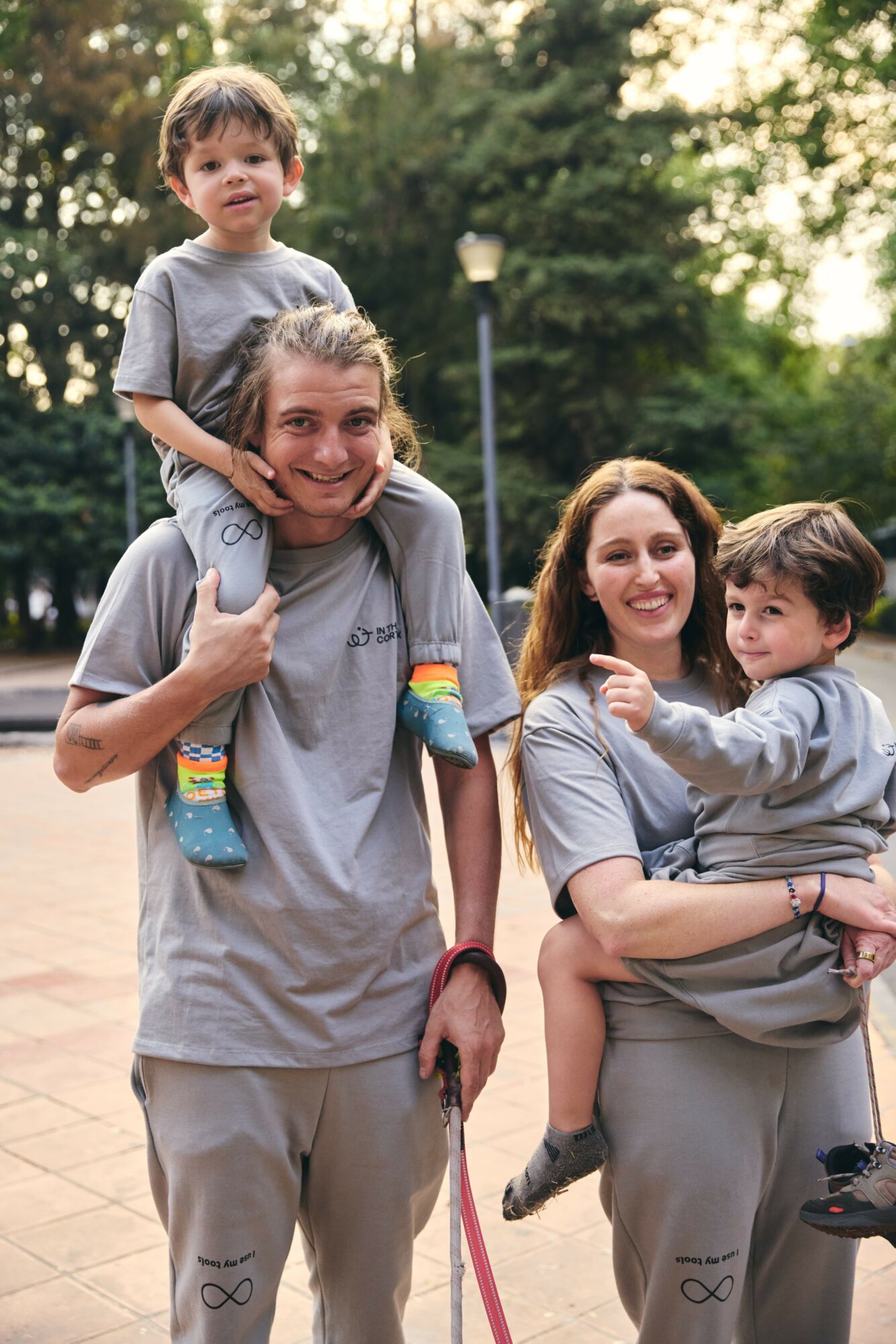 Two women and two children outdoors in a park, smiling, with trees and a lamppost in the background.