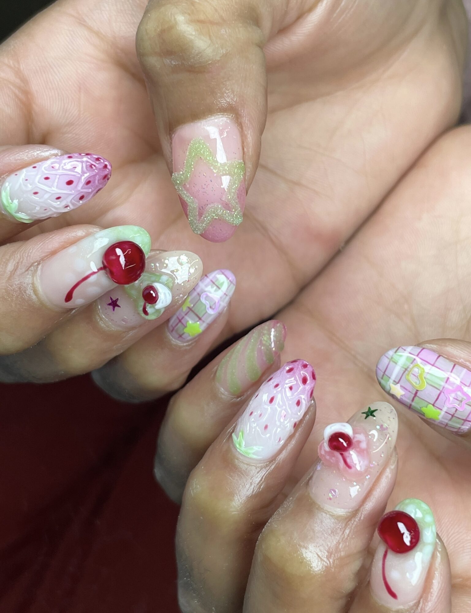 Close-up of hands with colorful, patterned nail art, including polka dots, plaid, and decorative elements like cherries and stars.