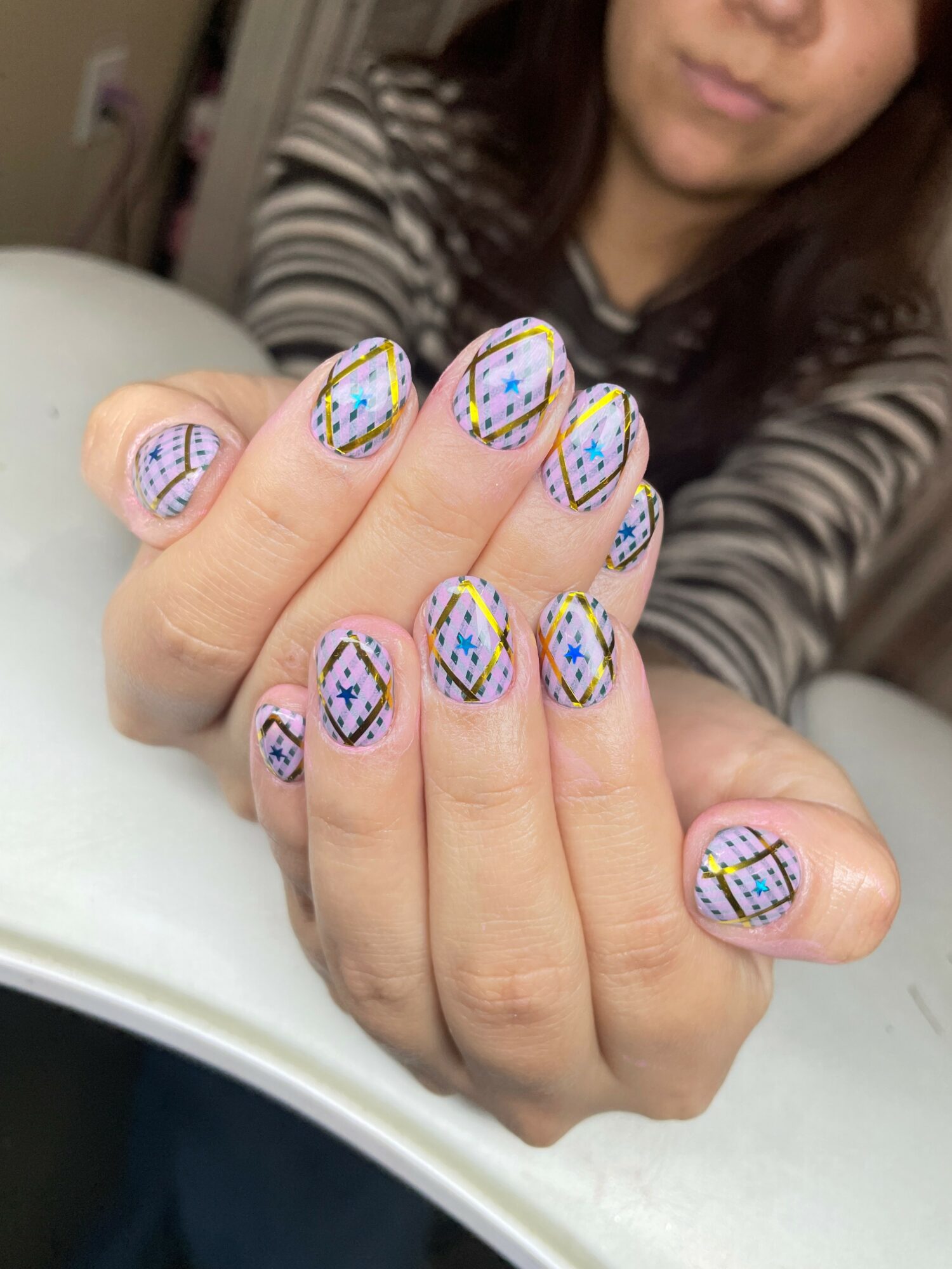 Person shows hands with colorful, patterned nail art, wearing a striped shirt, in an indoor setting.