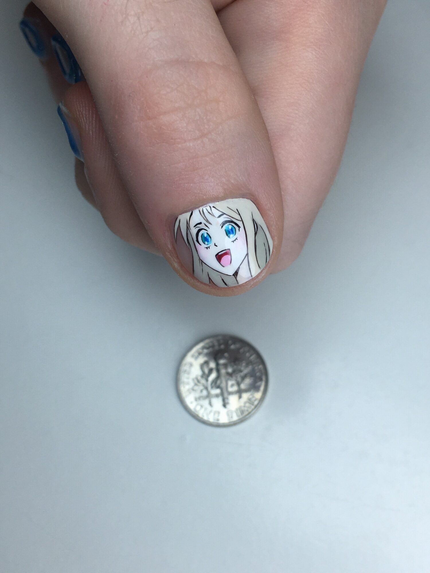 Nail with anime-style character with blonde hair and blue eyes, winking and smiling, next to a coin, on a white surface.