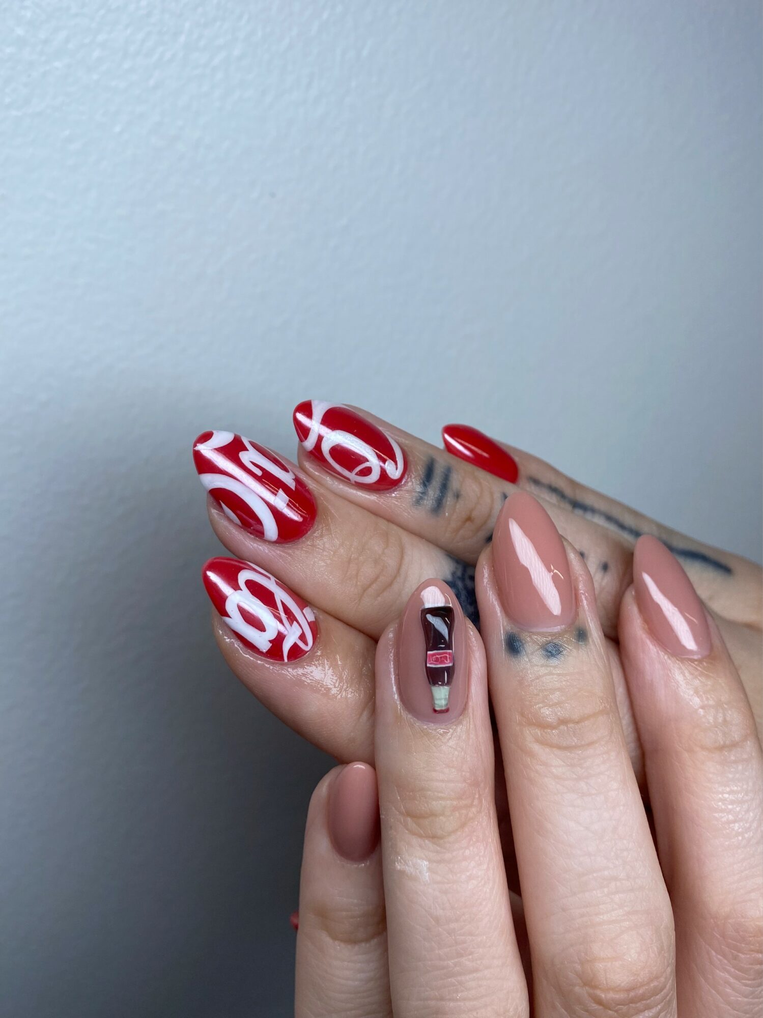 Hand with decorated nails, some painted red and others with black, white, and pink designs, against a plain background.