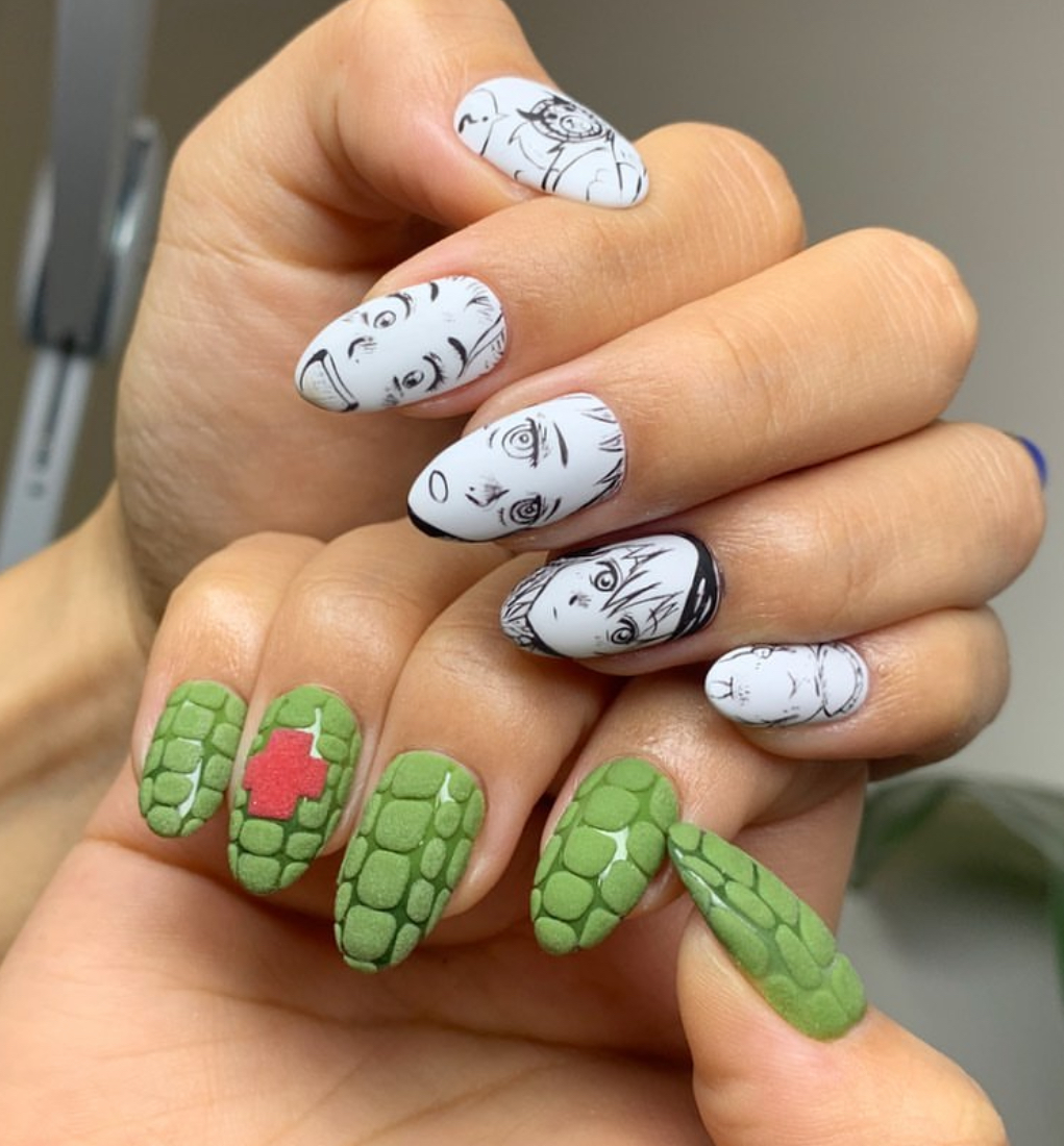 Hand with white nails featuring black line art faces and green nails with pink cross patterns, all in a close-up.