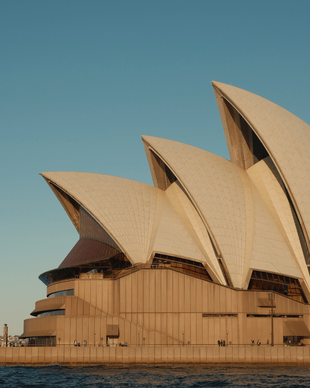 Sydney Opera House with a clear blue sky in the background, showing its distinctive sail-like roof structures.