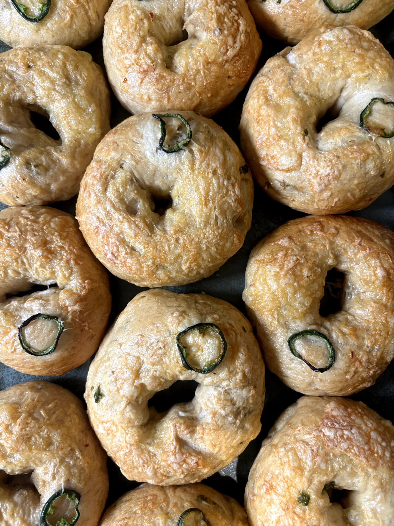 Close-up of baked bagels with a golden-brown crust and green jalapeño slices on top.
