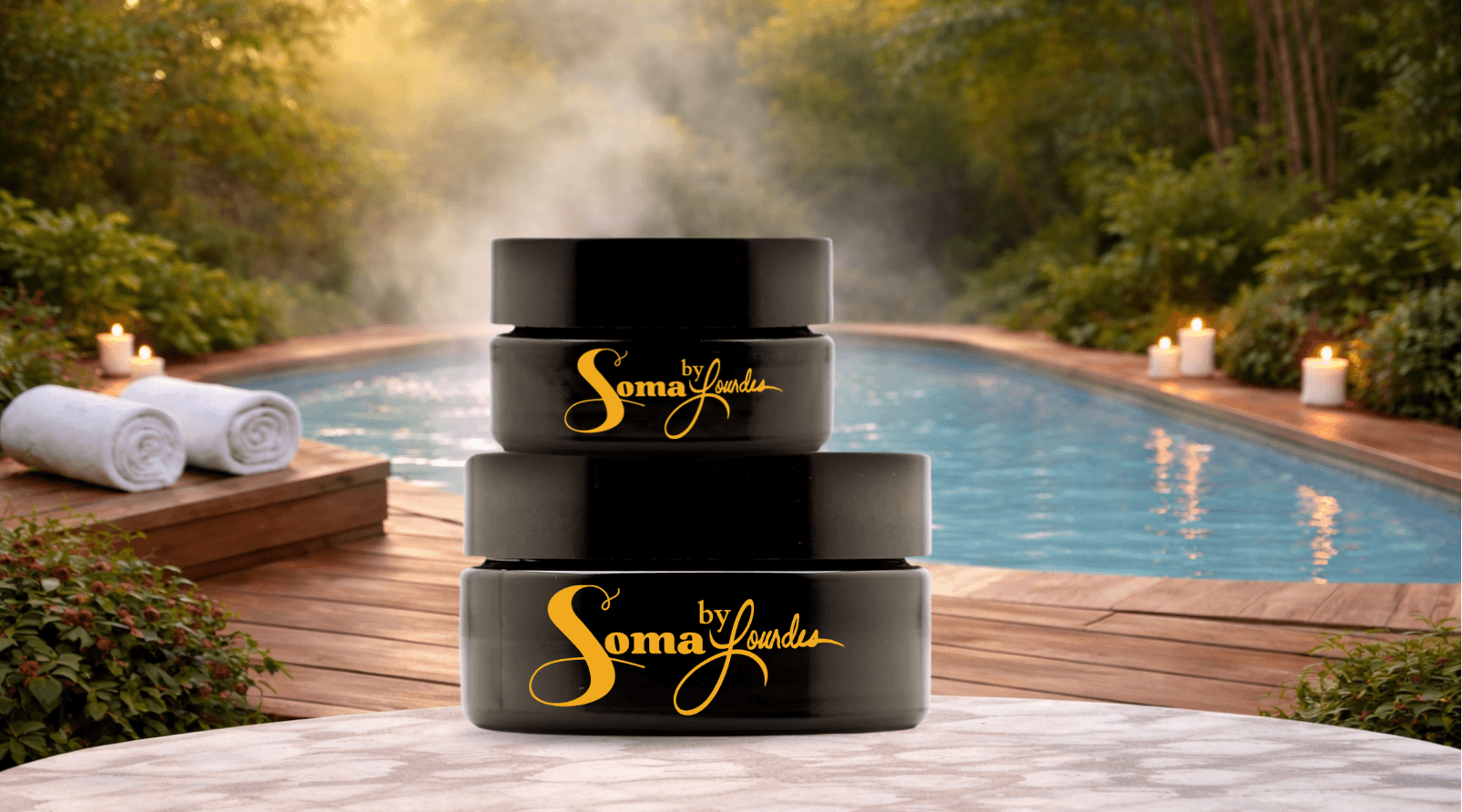 Three black containers with gold text stacked outdoors near a pool, candles and towels in the background.