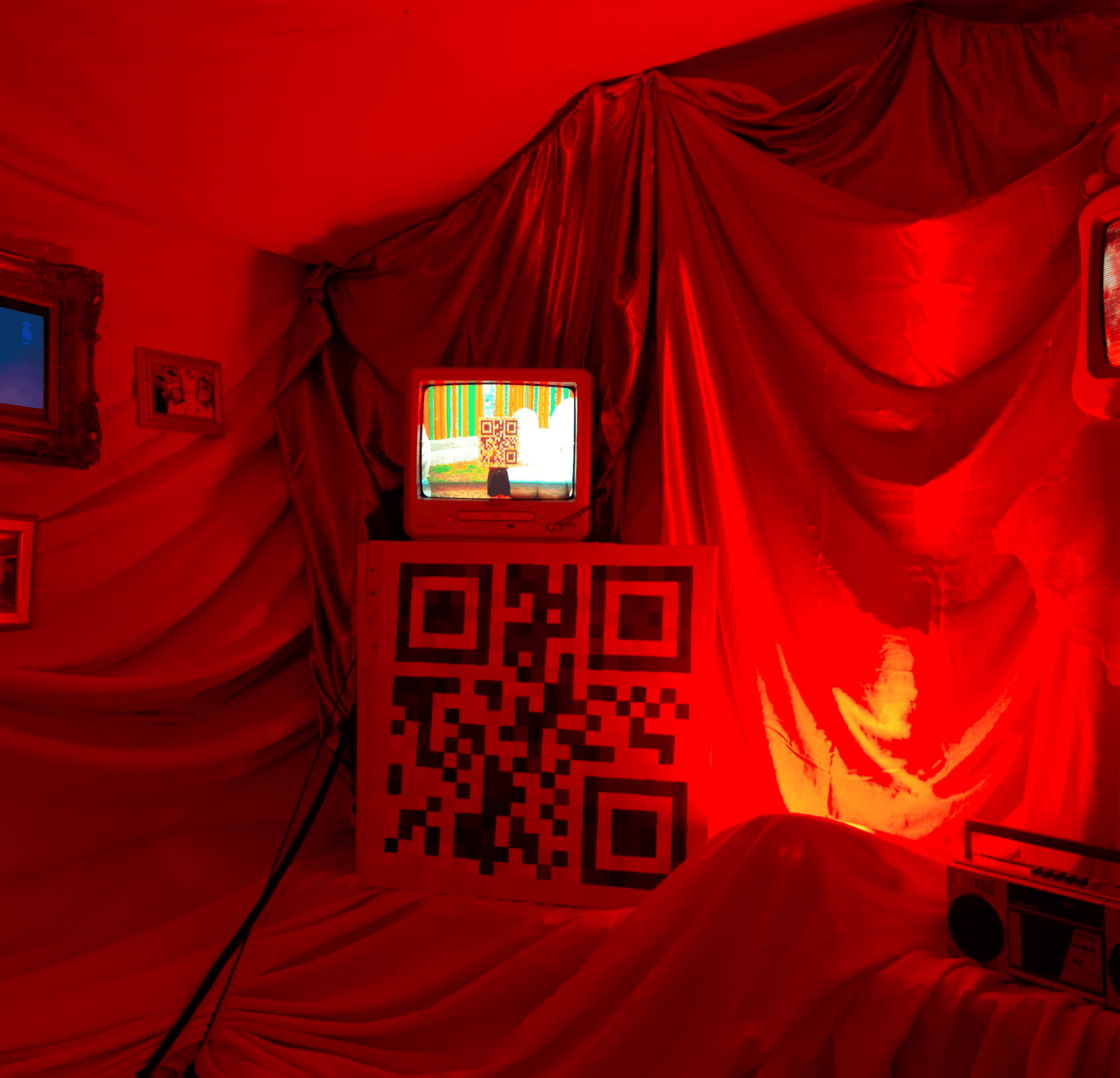 Room with red drapes, a small TV on a stand with a QR code, and a radio, all bathed in red light.