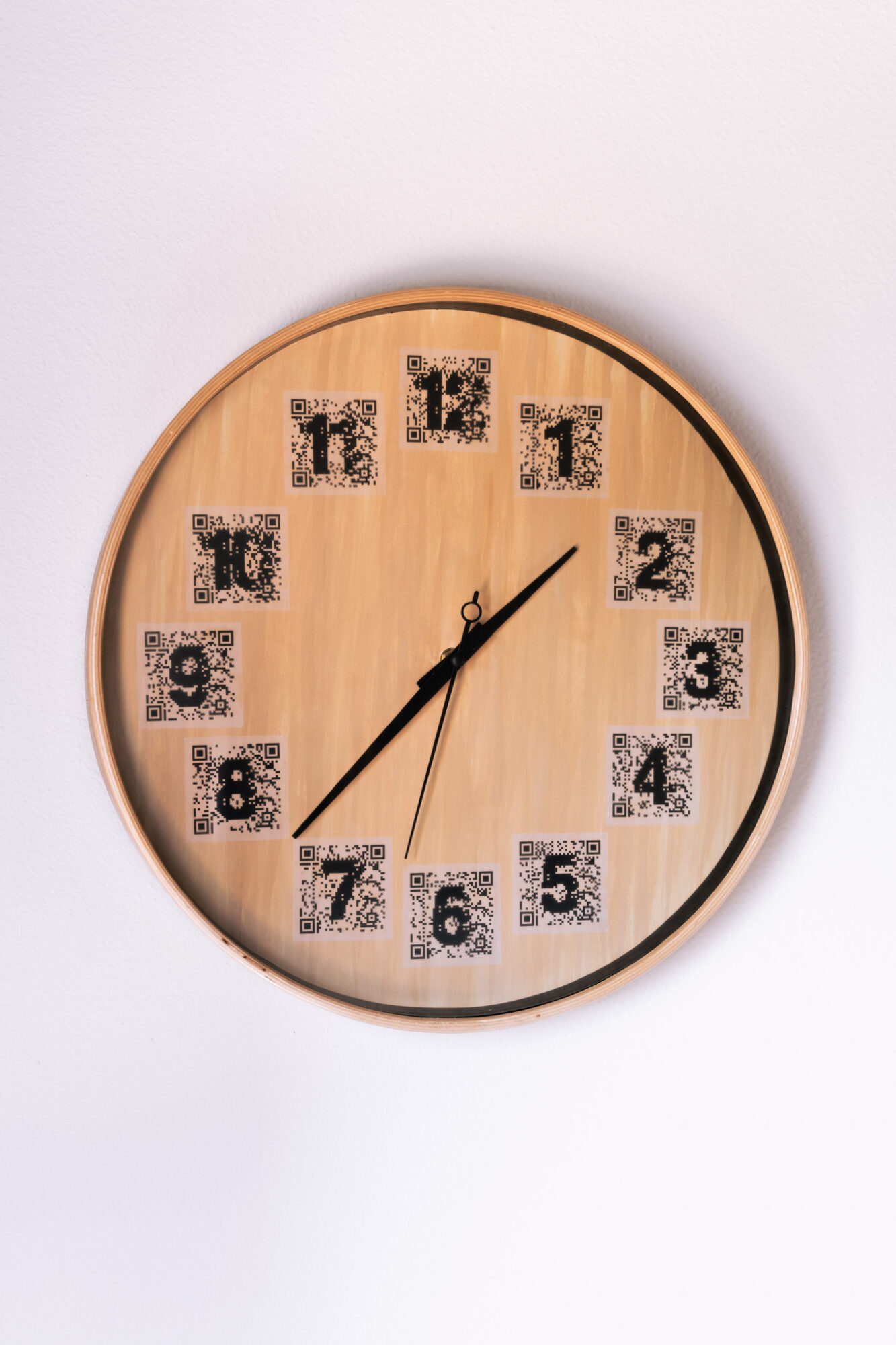 Round wooden clock with black and white patterned numbers and black hands showing 1:10.