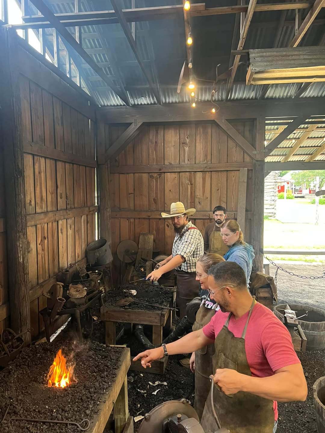 Four people working with tools inside a wooden workshop, one person in a pink shirt in the foreground, others in the background.