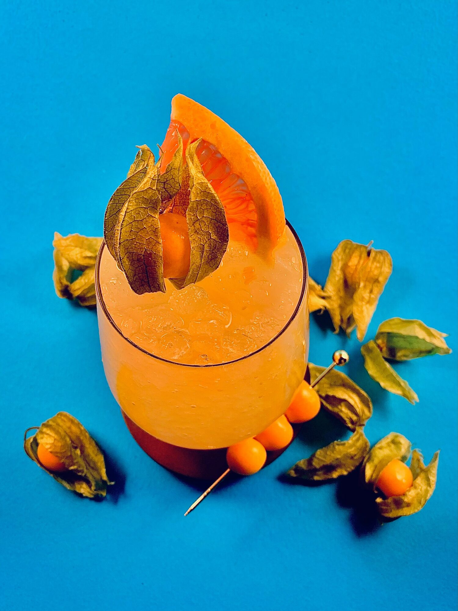 A glass of orange juice with a slice of orange and dried fruit garnishes on a blue background.