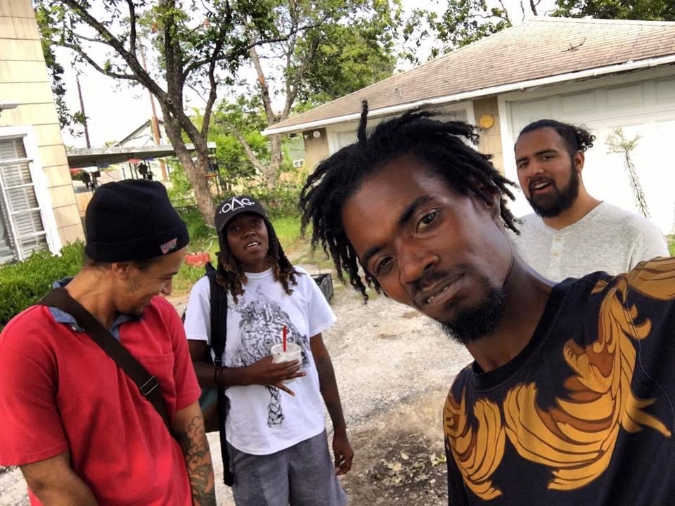 Group of four people outdoors, one taking a selfie, with trees and a house in the background.