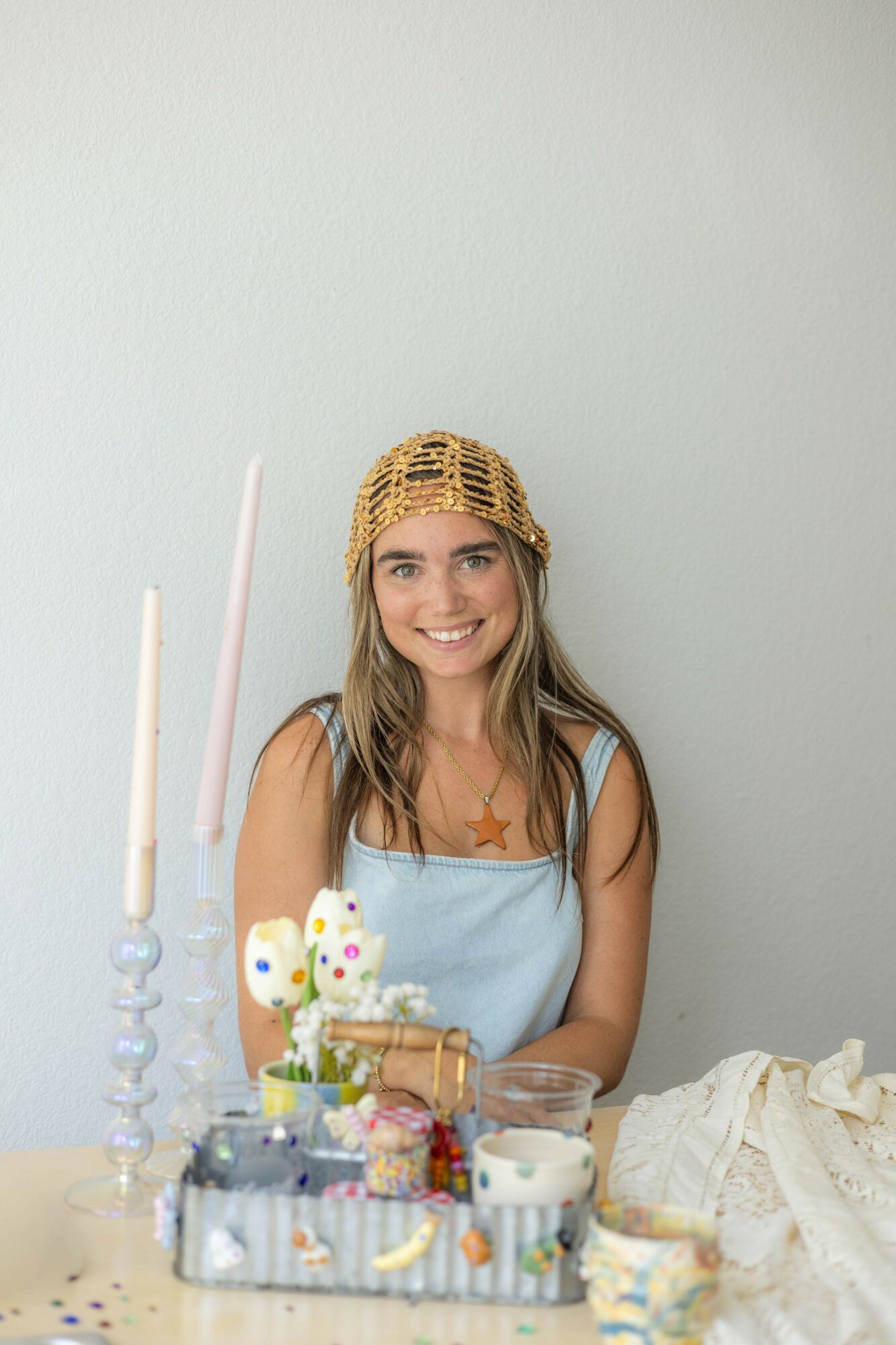 Smiling girl wearing a gold crown and star-shaped necklace, sitting at a table with decorated cupcakes and candles.