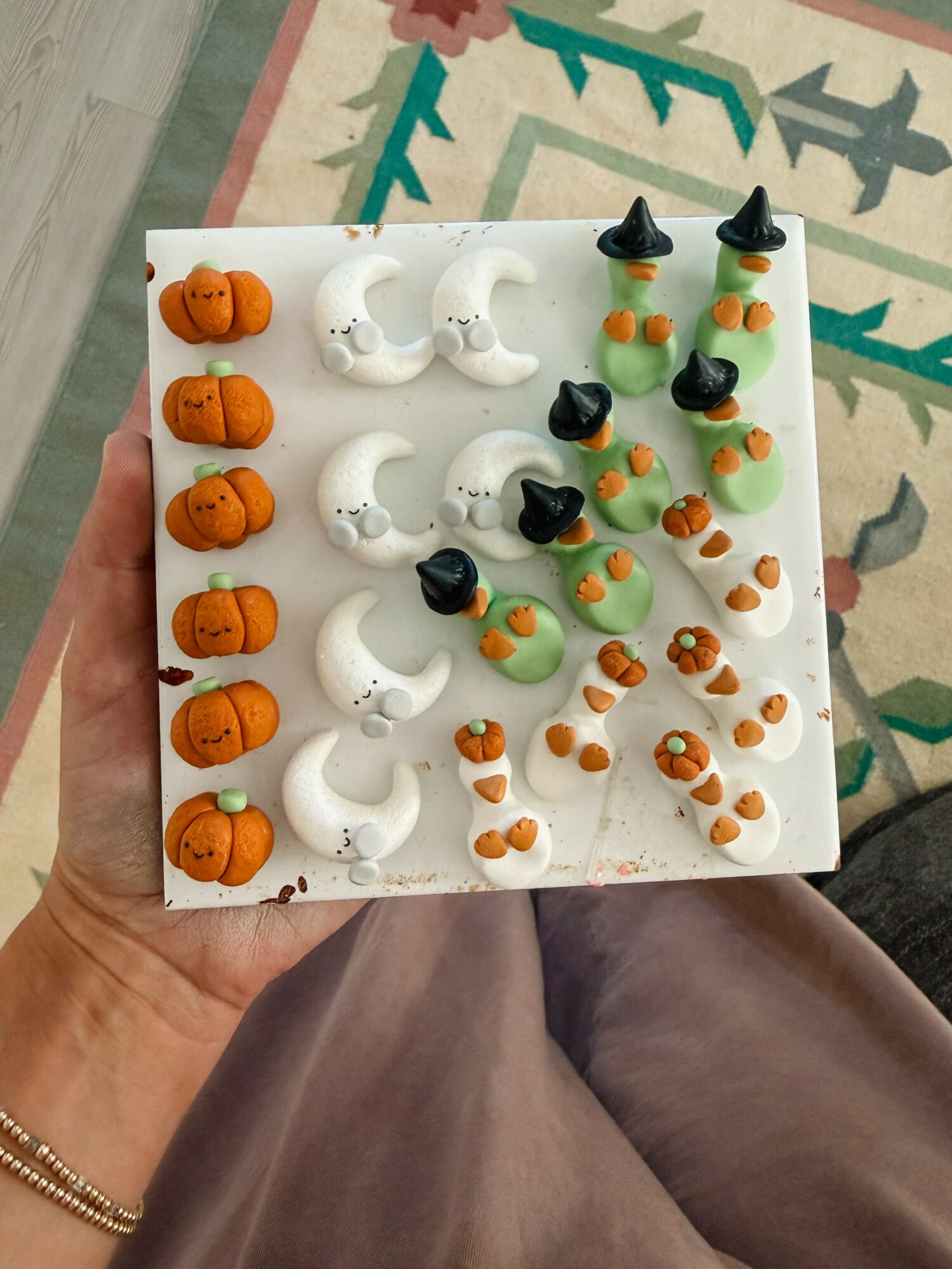 Assorted Halloween-themed cake decorations including pumpkins, ghosts, witches' hats, and candy corn on a white square board.