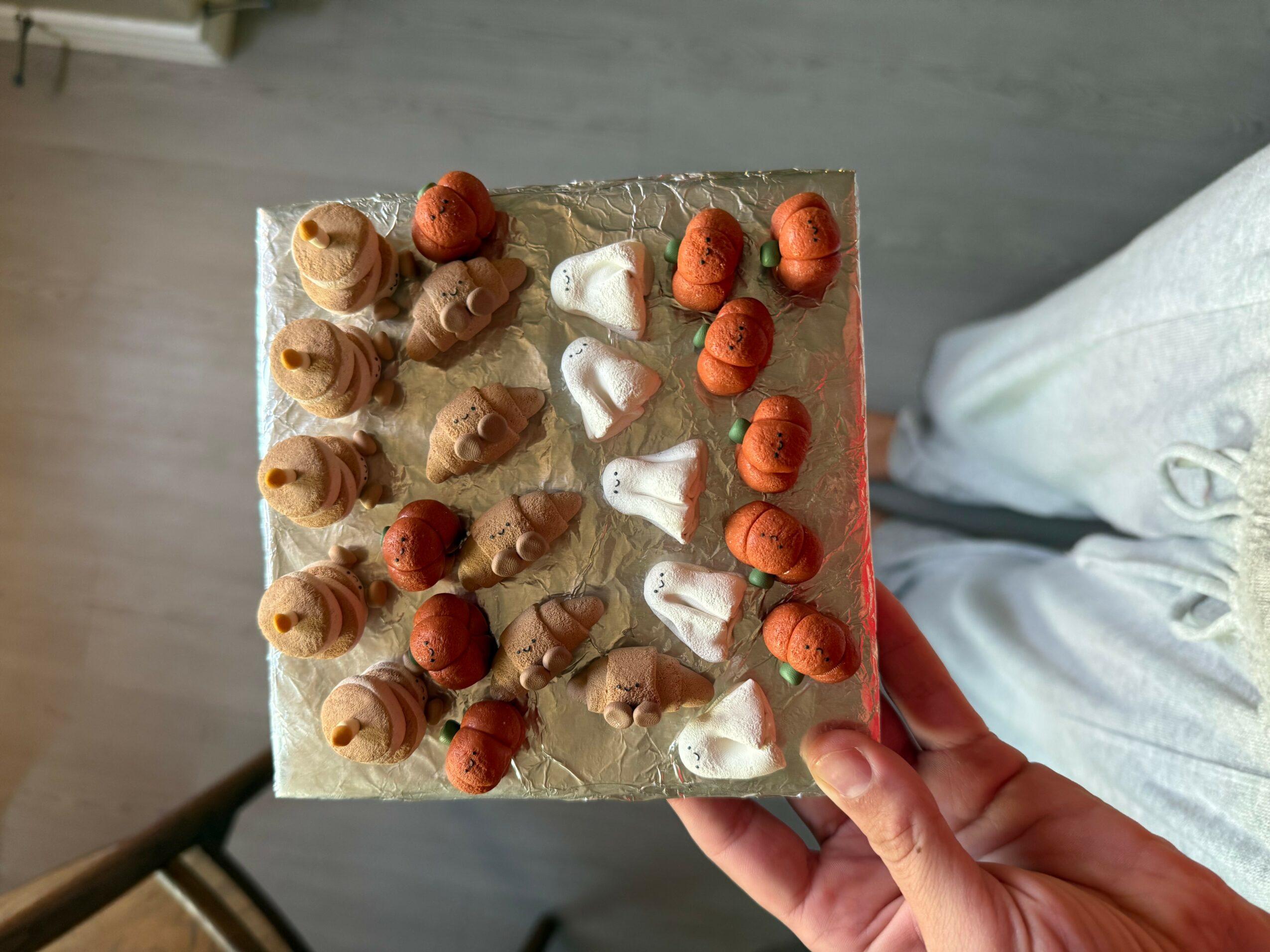 Hand holding a square tray with assorted ice cream cones and scoops, some with toppings, on a gray surface.