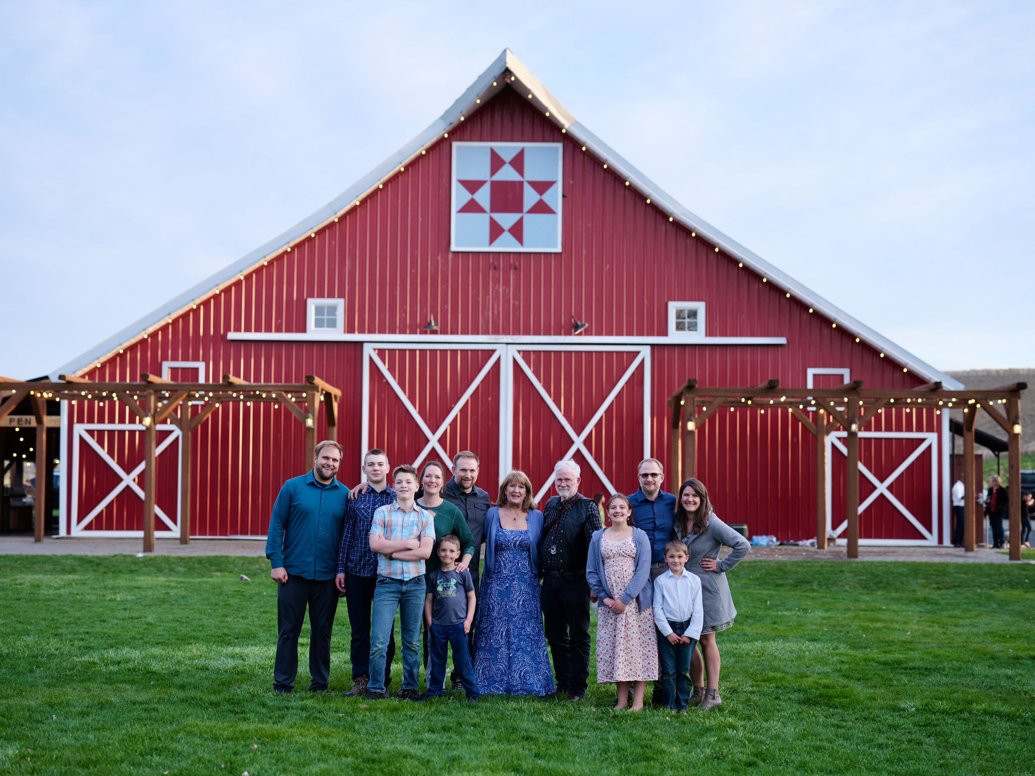 Group of people standing in front of a large red barn with white accents, under a clear sky.