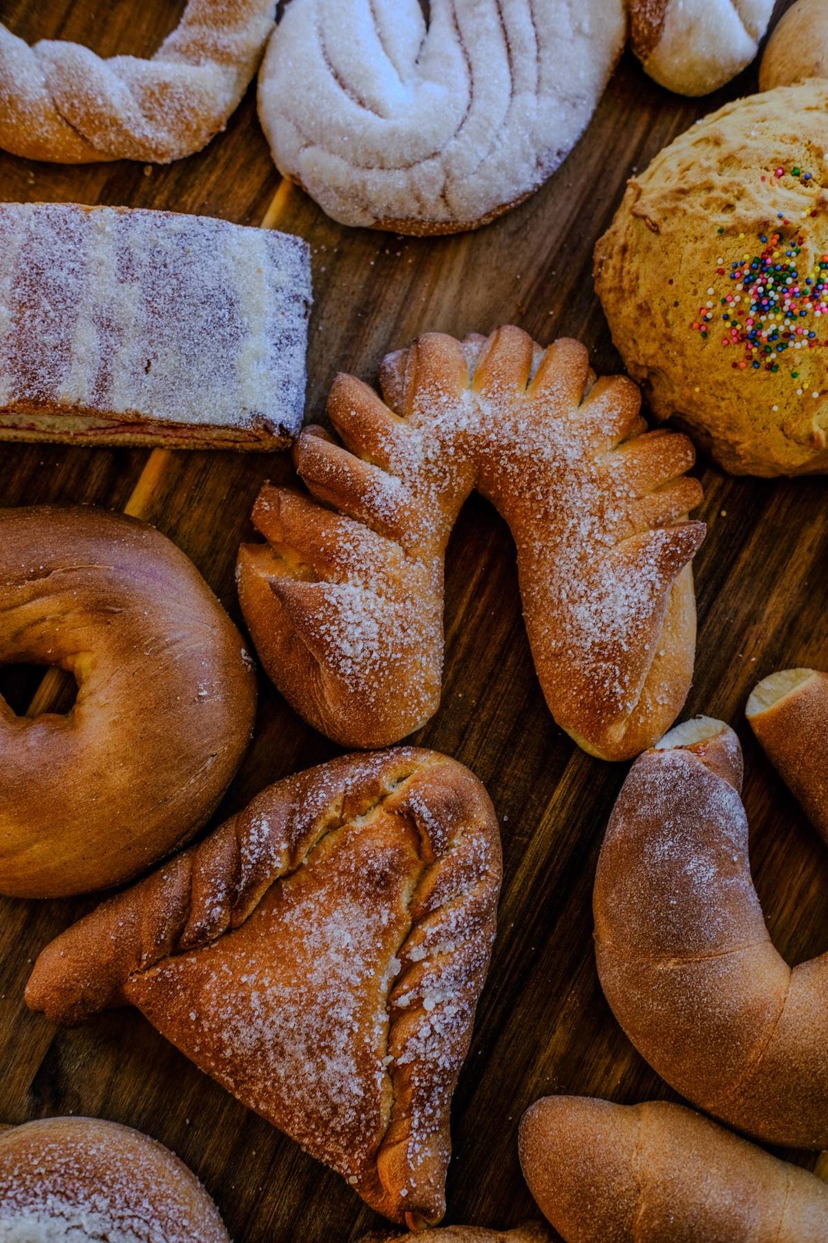 Assorted baked goods including cookies, bread, and pastries on a wooden surface.