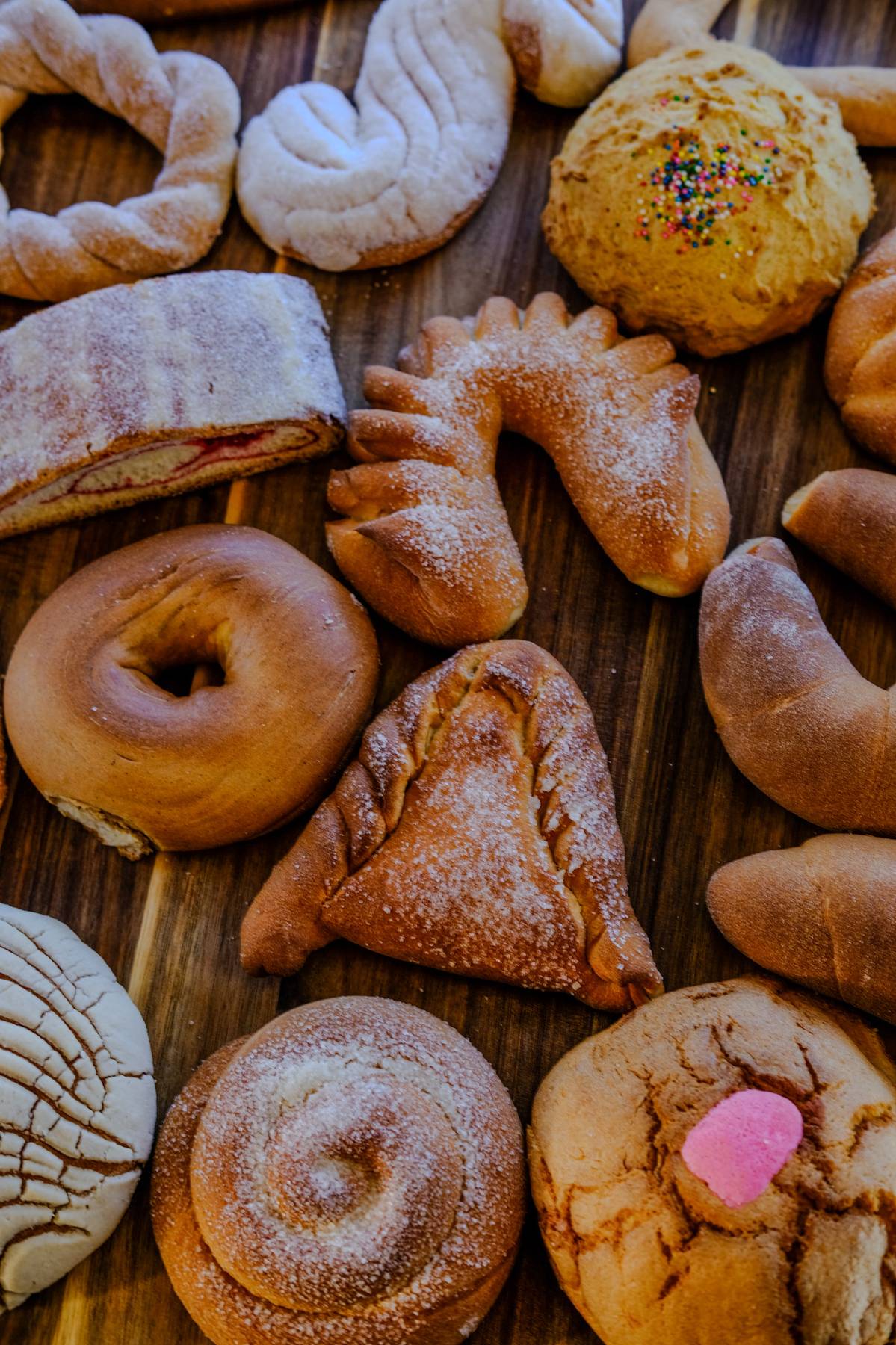 Assorted baked goods including cookies, croissants, muffins, and pastries on a wooden surface.