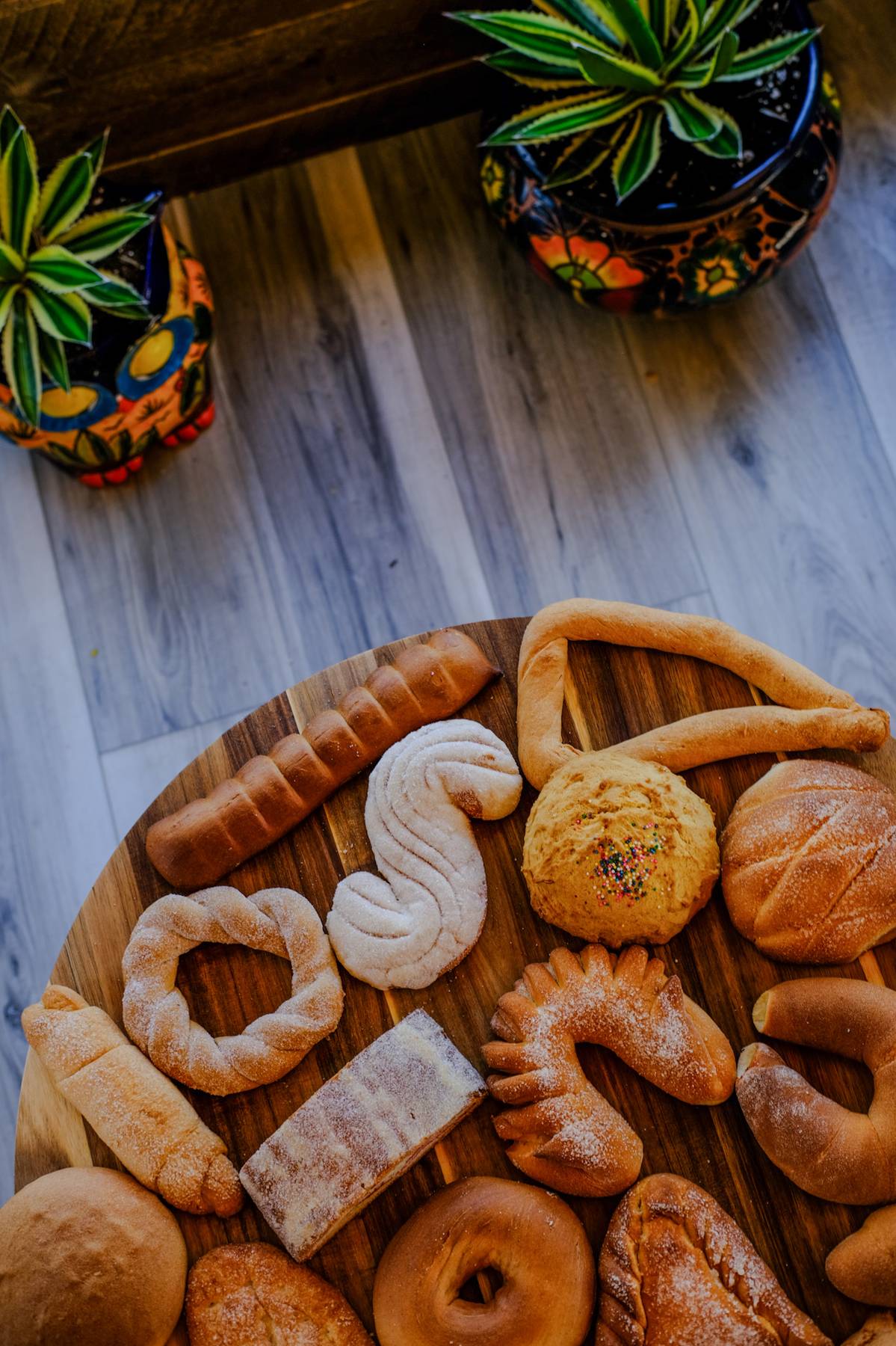Assorted baked goods on a wooden tray, with potted plants in the background, on a wooden floor.