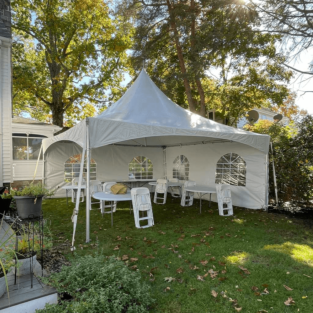 White outdoor tent set up on a grassy lawn with trees in the background, sunlight filtering through leaves.