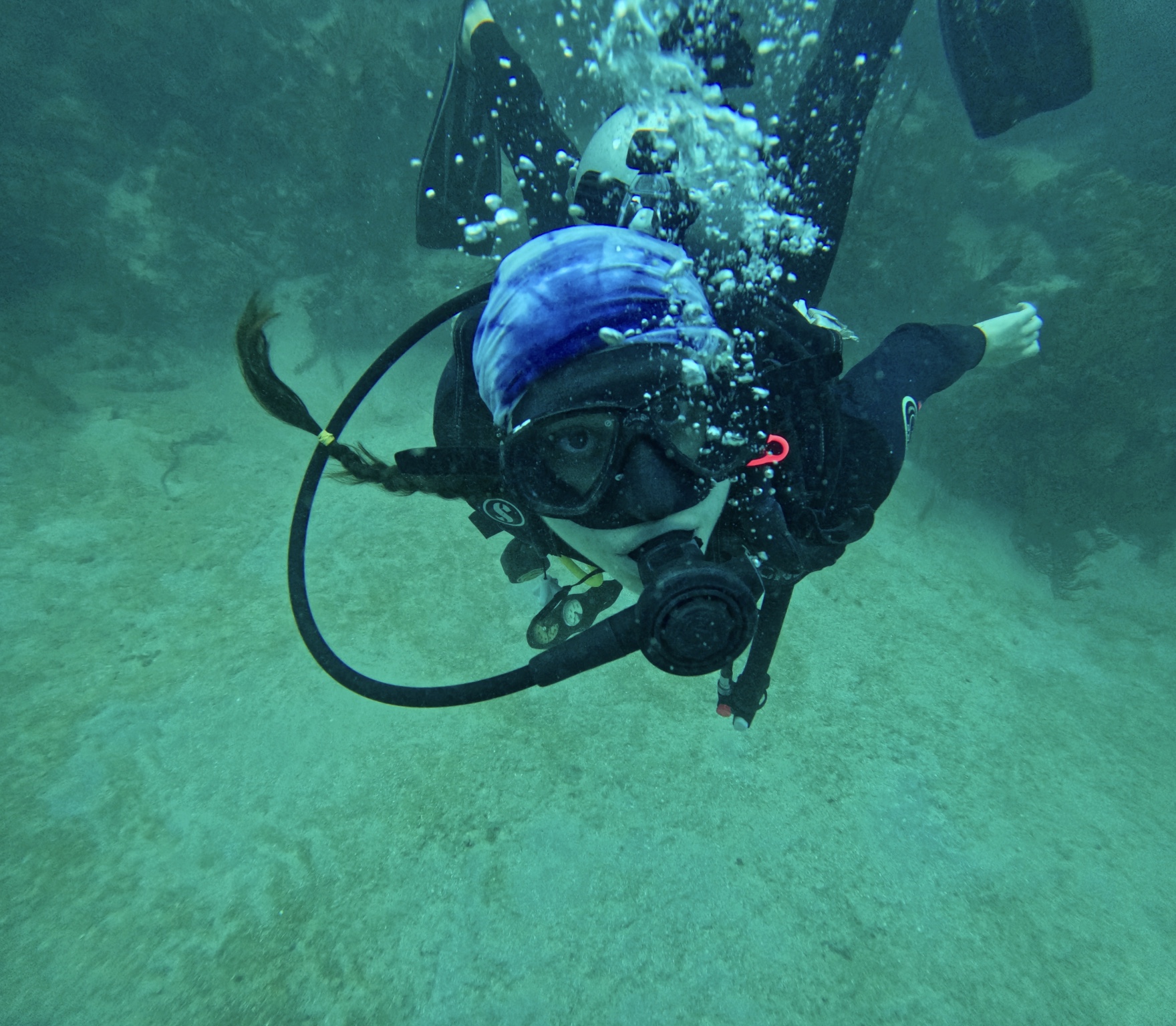 Person scuba diving underwater, wearing a mask, snorkel, and wetsuit, with bubbles around them.