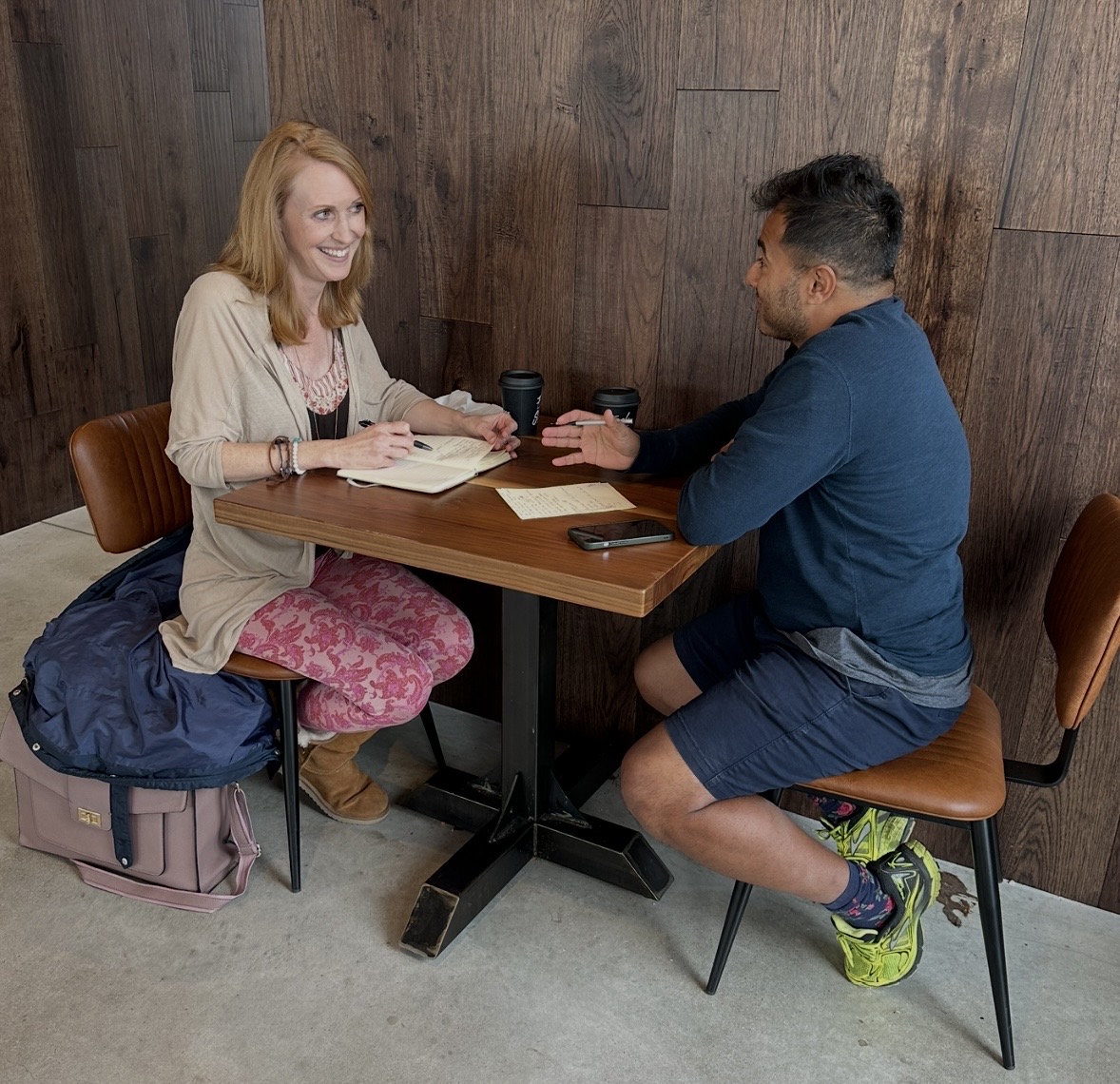 Two people sitting at a table, talking and smiling, in a room with wooden walls.