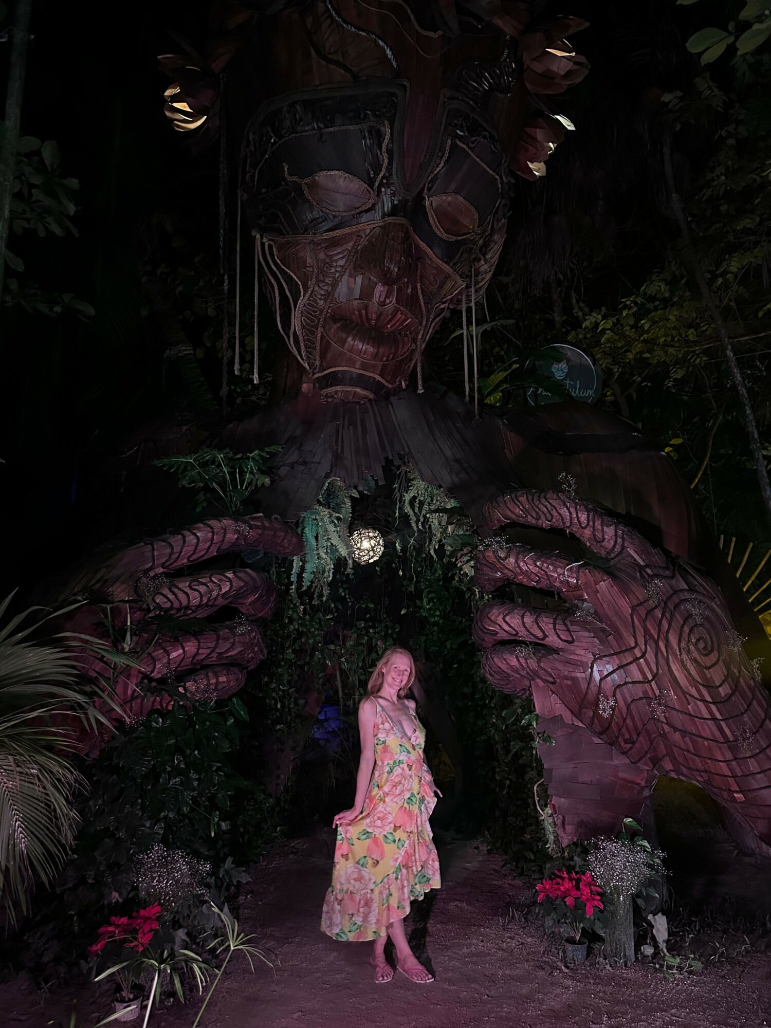 Person in traditional attire and a child in a pink dress in a garden with plants and flowers.