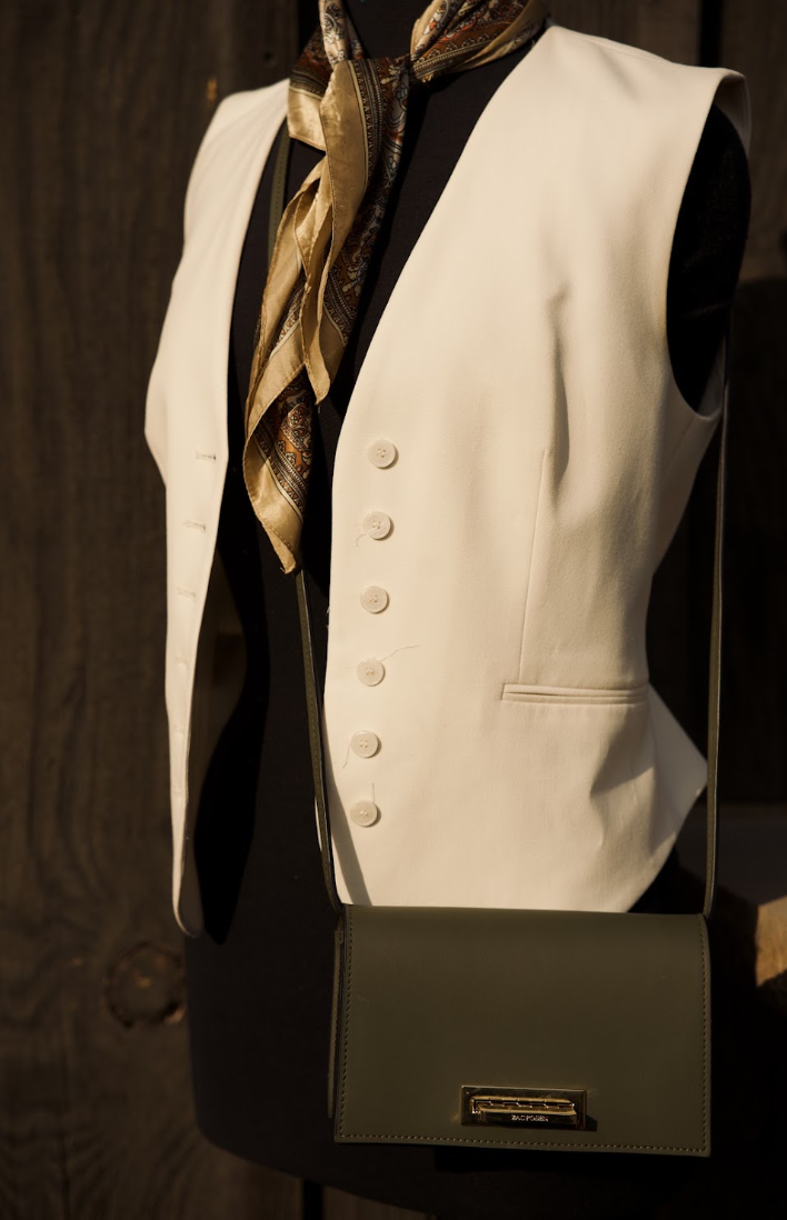 Close-up of a mannequin wearing a white sleeveless vest over a black outfit, with a gold and black patterned scarf, and a black purse.