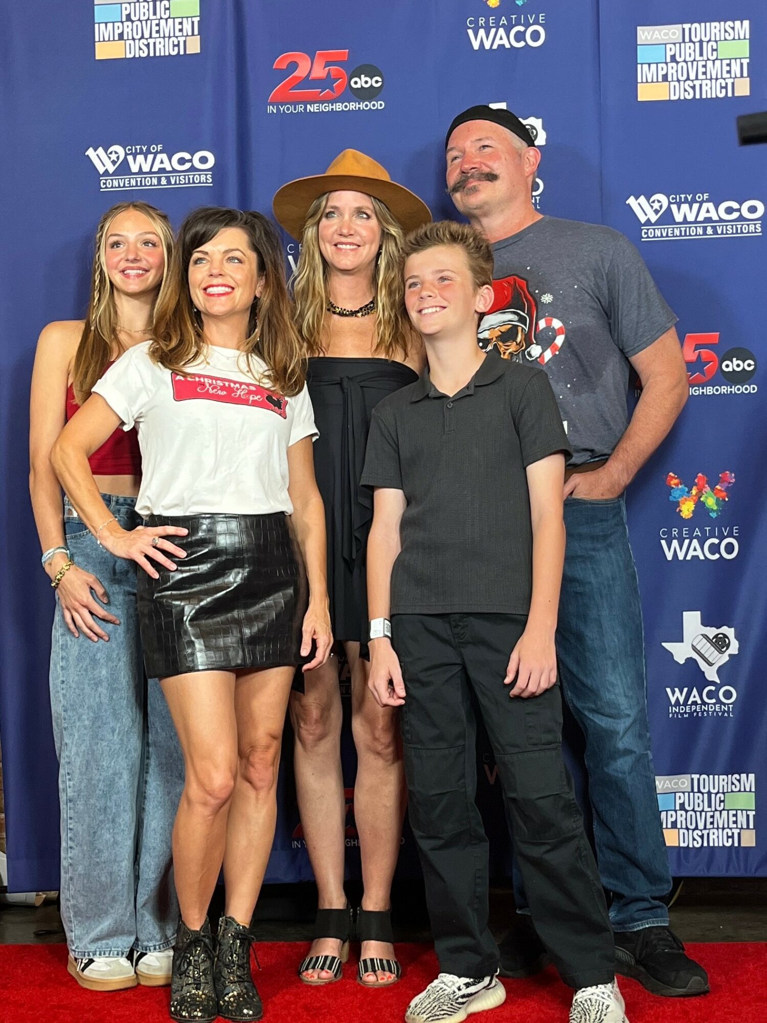 Group of five people smiling on red carpet in front of blue backdrop with logos, including Waco and ABC. Four females and one male, all casually dressed.
