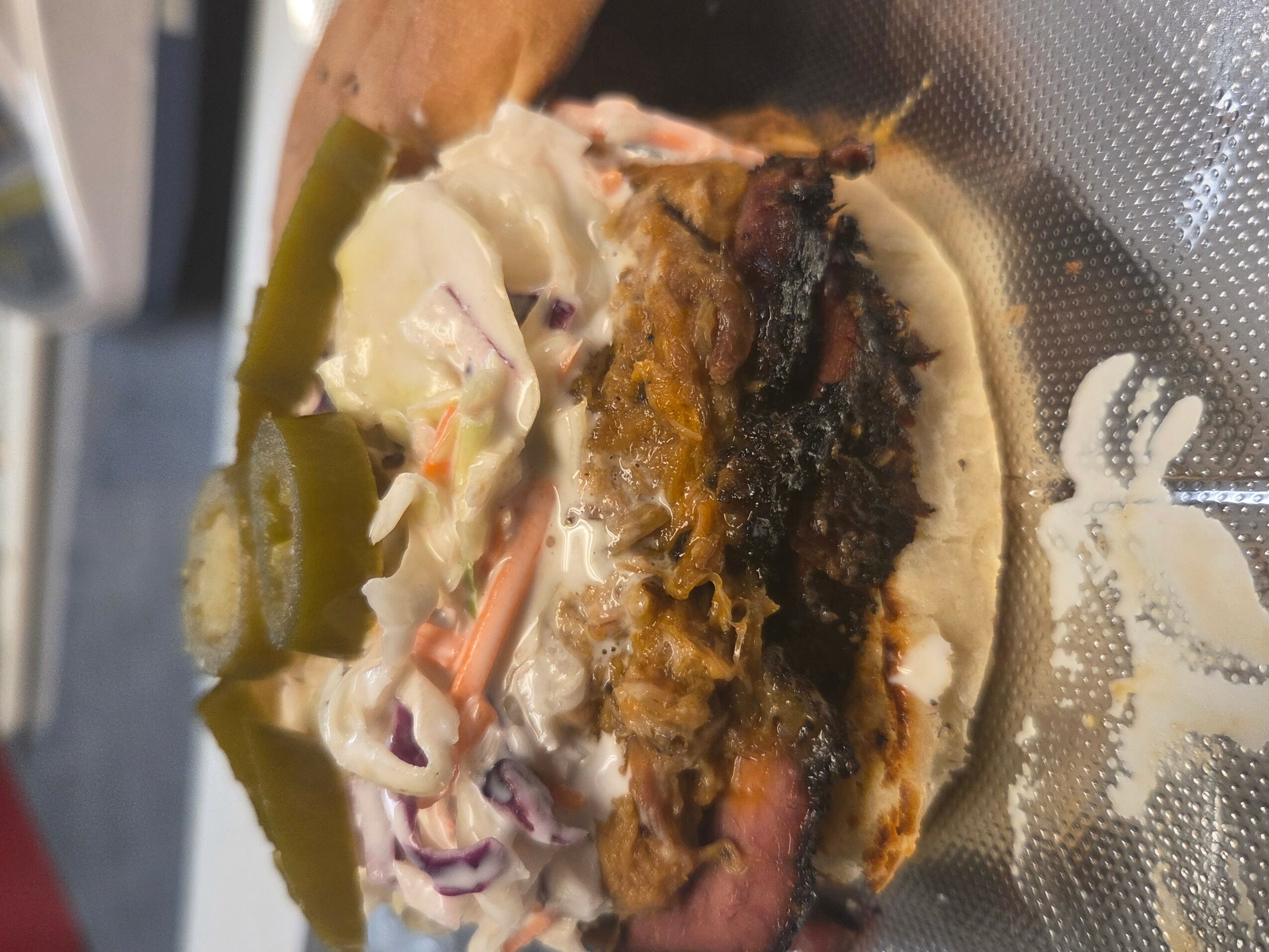 A sandwich with pickles, coleslaw, and a fried patty, partially eaten, on a paper wrapper.