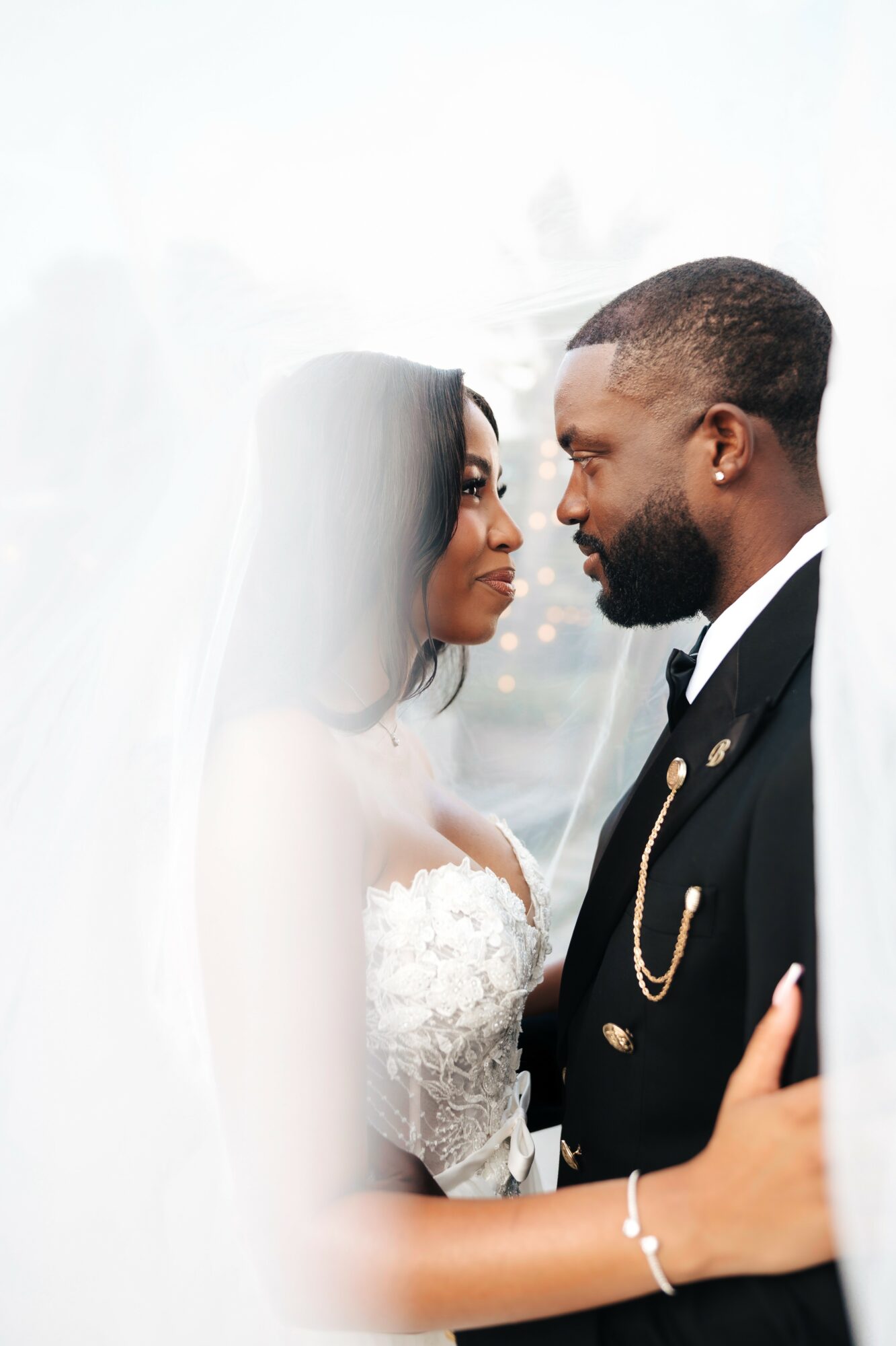 Bride and groom face each other closely, smiling, with wedding attire, in a bright setting.