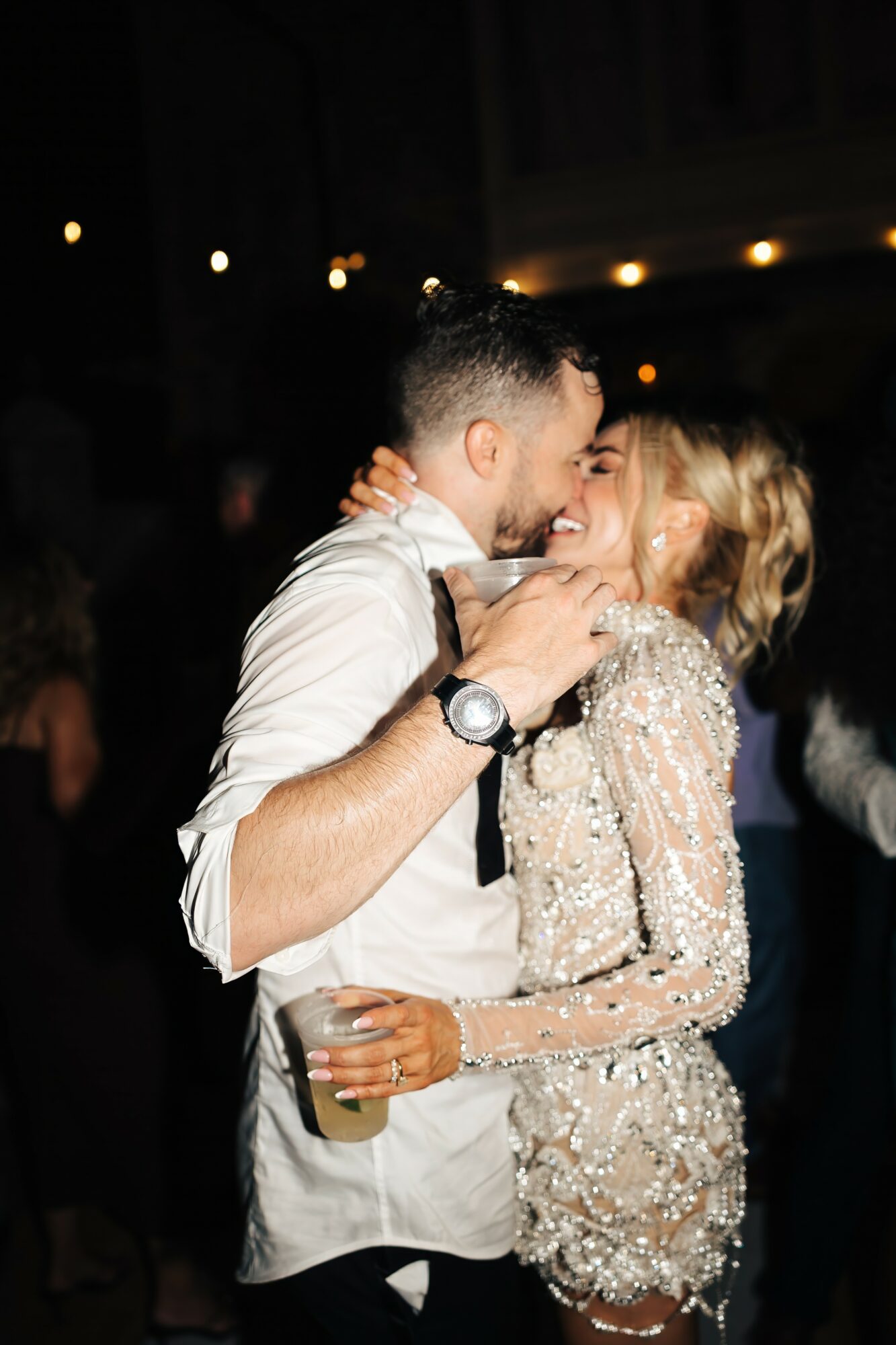 A couple dancing closely at a party, with the man holding a drink and smiling, and the woman smiling back.