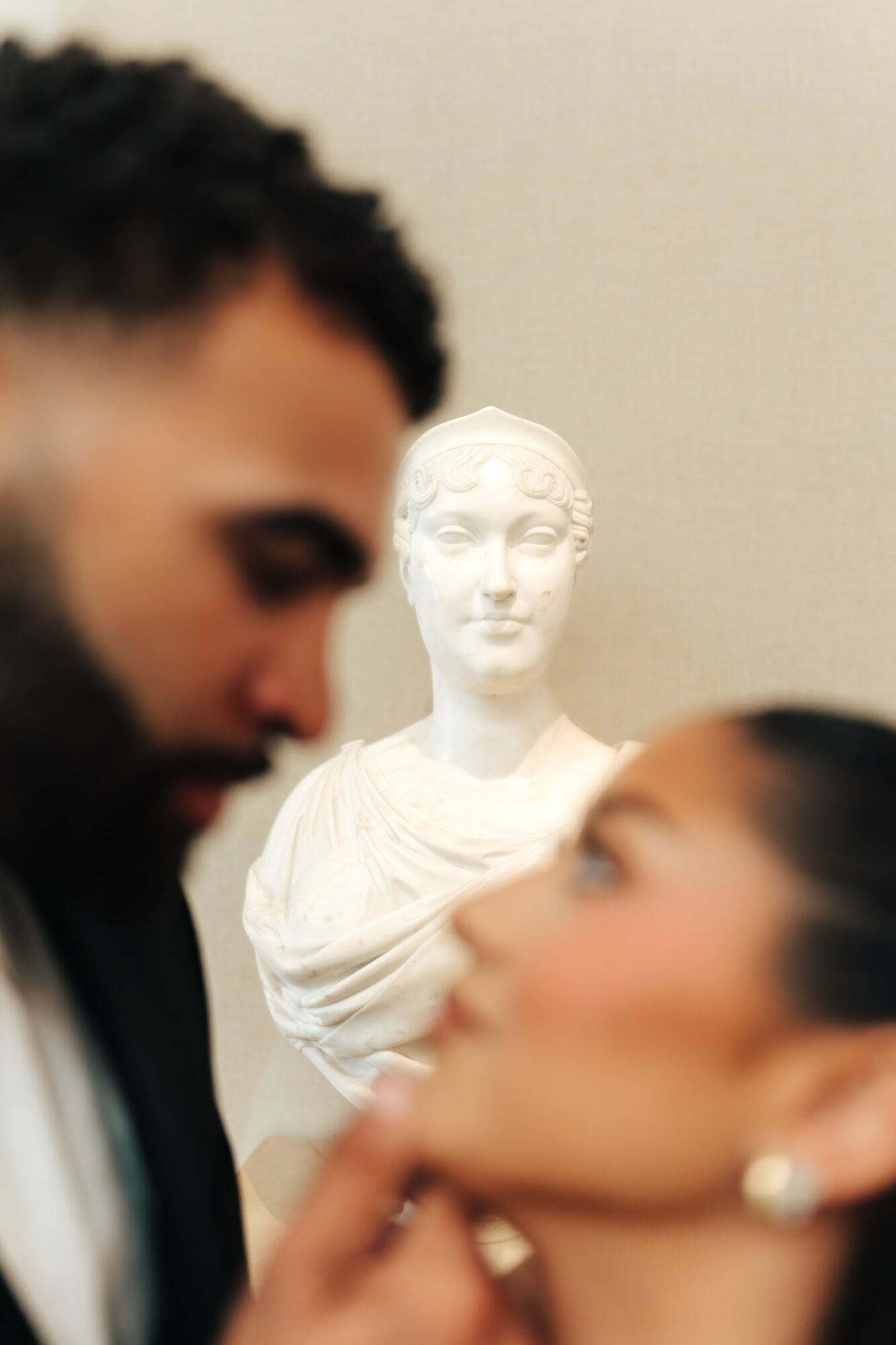 Blurred man and woman in foreground with a white classical bust sculpture in background.