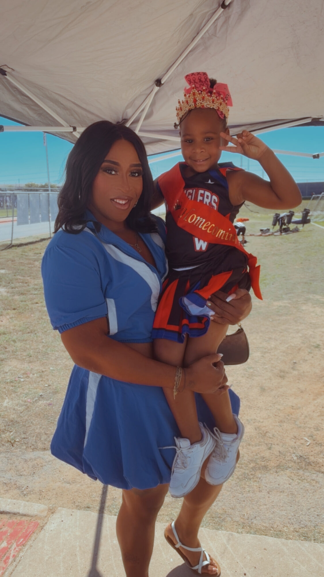 Woman holding a young boy under a tent, boy wearing a crown of snacks, both smiling outdoors.