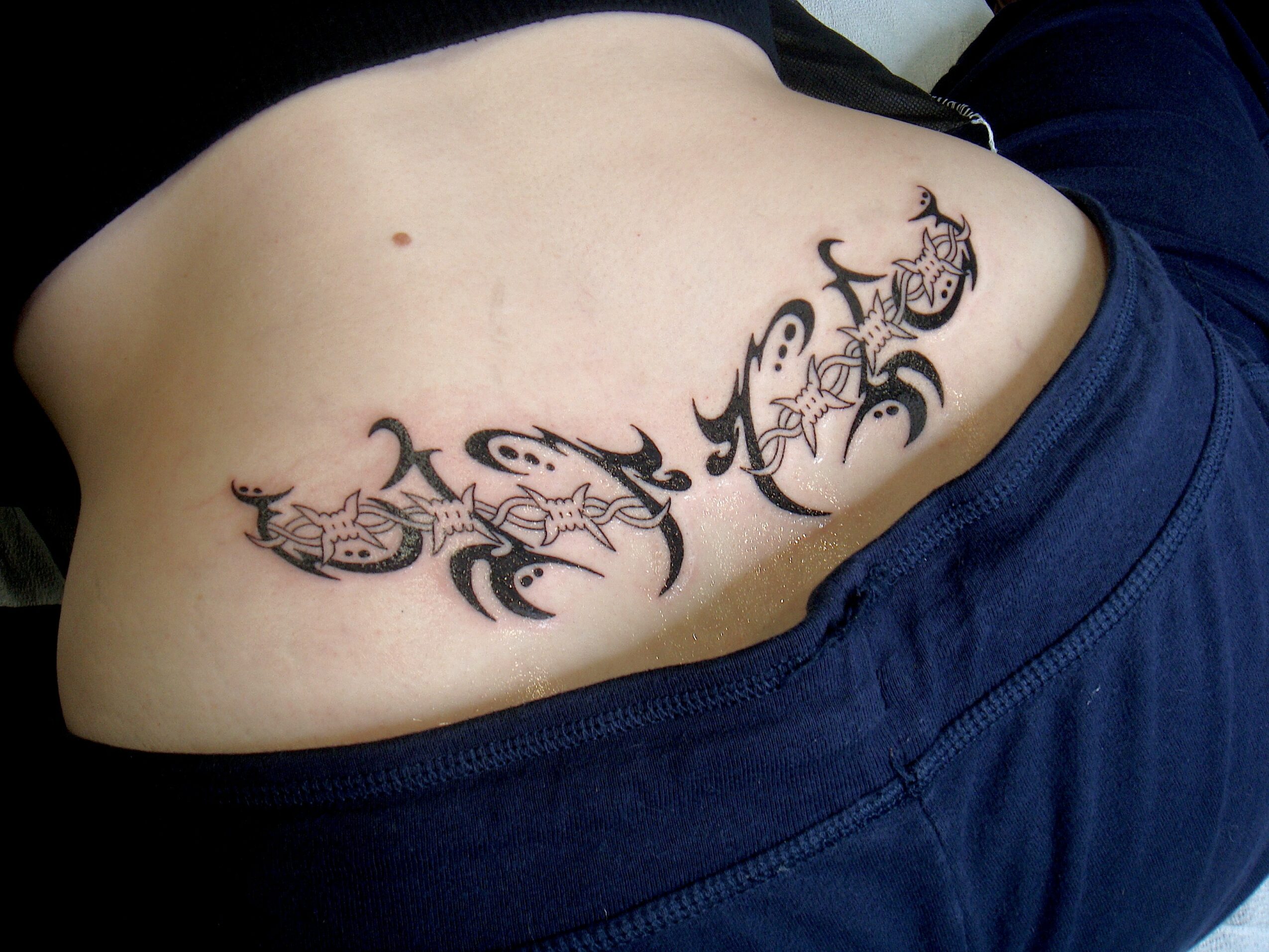 Tattoo of tribal-style designs on person's side near waist, with skin visible and clothing partially shown.