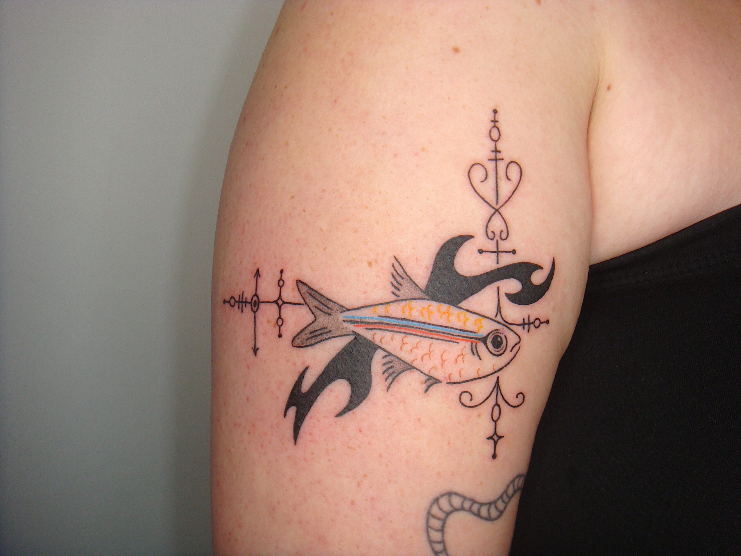 Tattoo of a fish with a bird above it, decorated with ornate lines and symbols on upper arm.