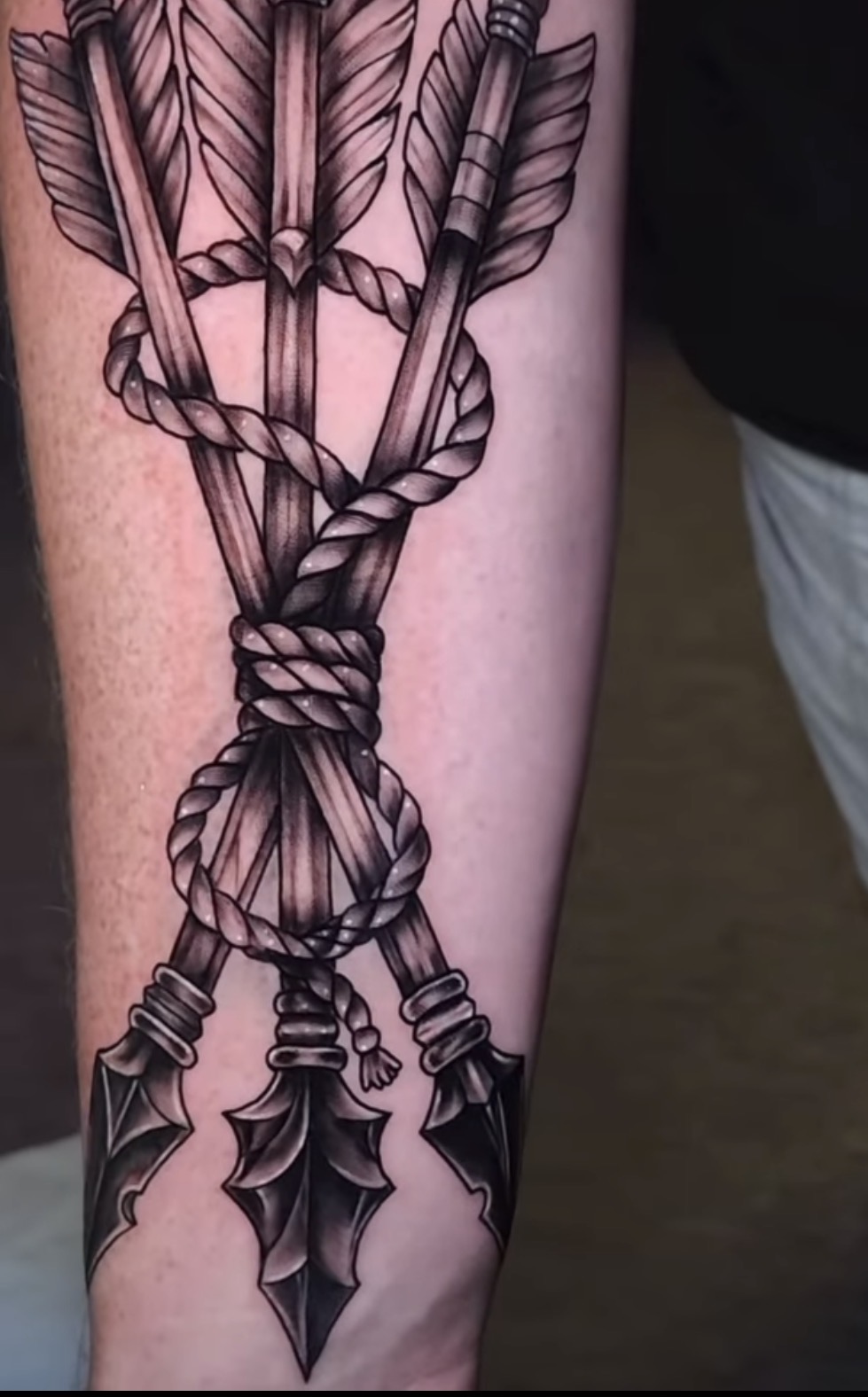 Tattoo of arrows wrapped in a rope, with arrowheads at the bottom, on a person's arm.