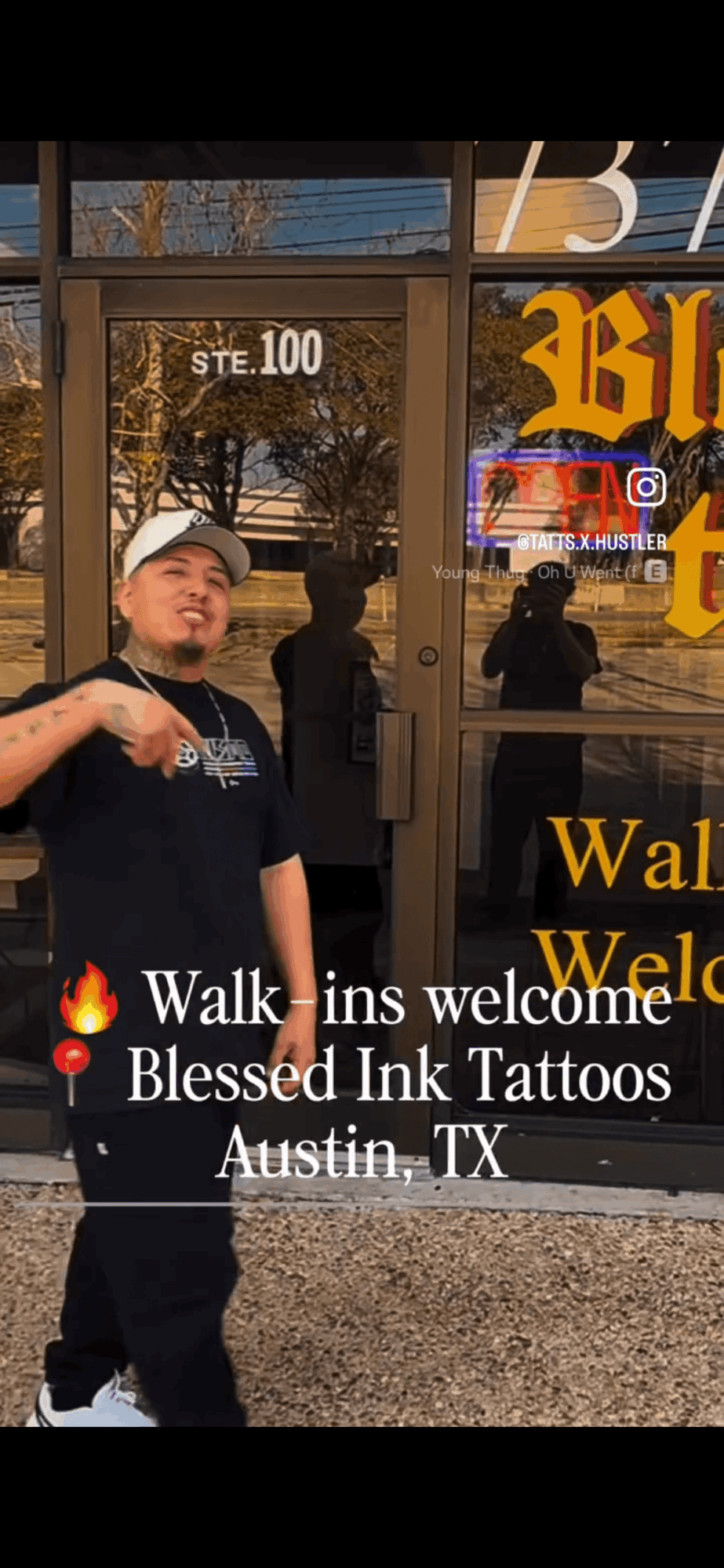 Person standing outside tattoo shop with glass door, reflection of street scene, and welcoming message on window.