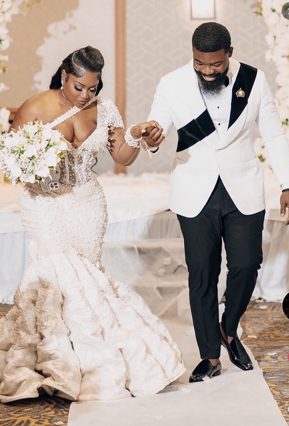 A bride and groom holding hands during their wedding ceremony, with the bride holding a bouquet of flowers, in an elegant setting.