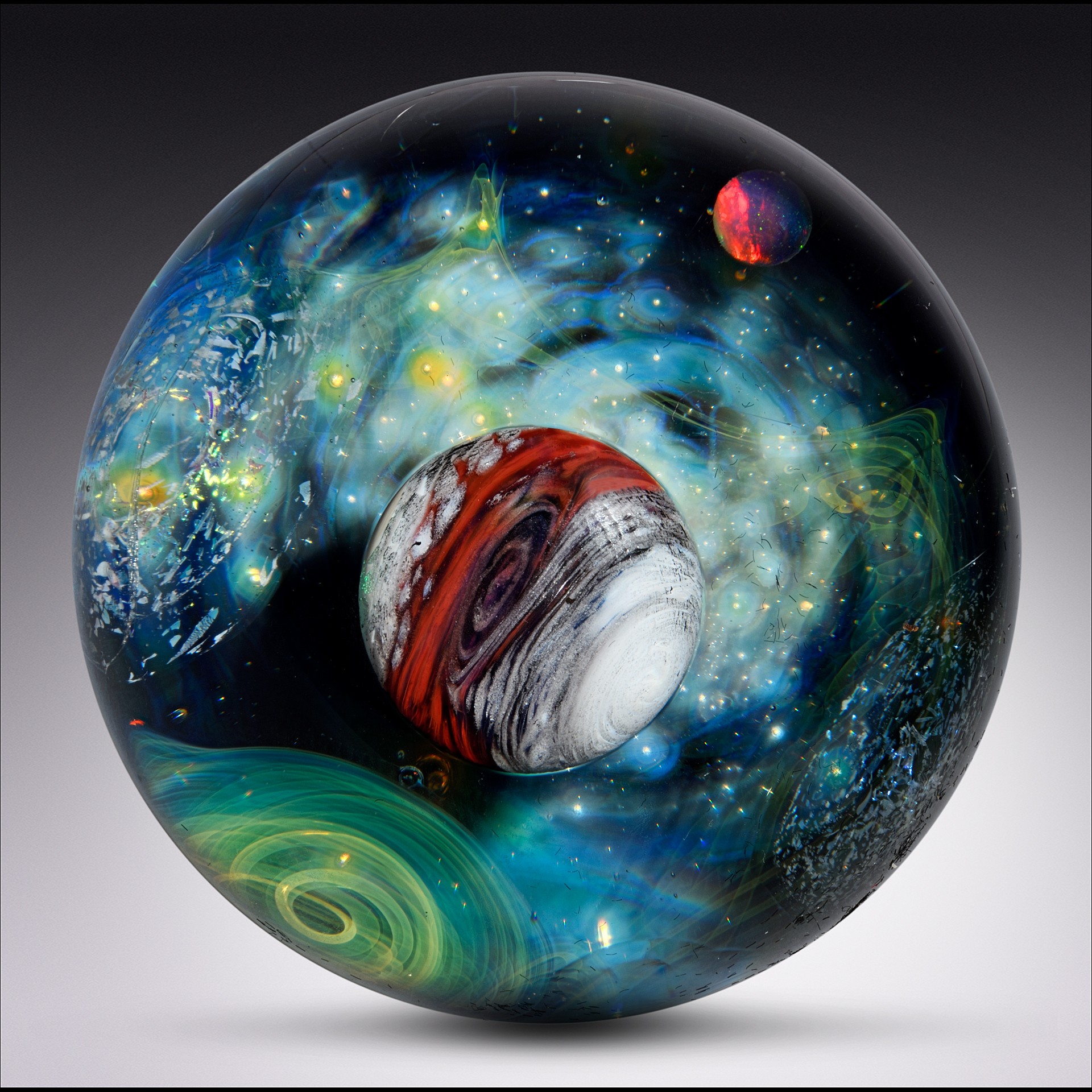Glass sphere with colorful galaxy and planet designs inside, including a red and white striped planet, against a gray background.