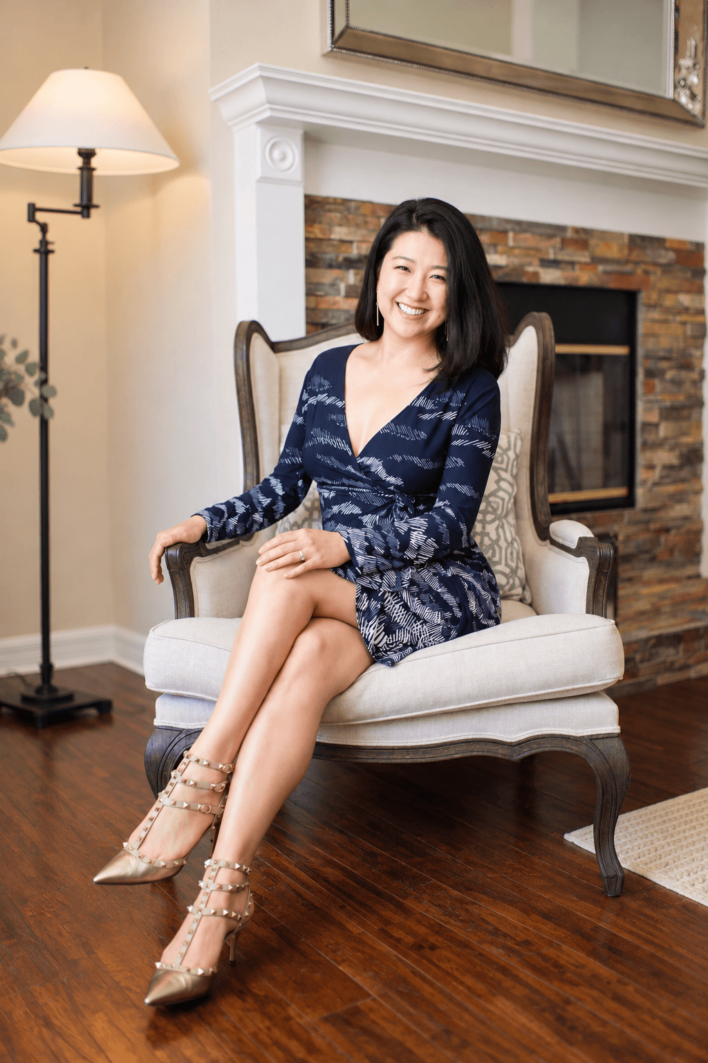 A person sits in an upholstered chair beside a stone fireplace in a living room.
