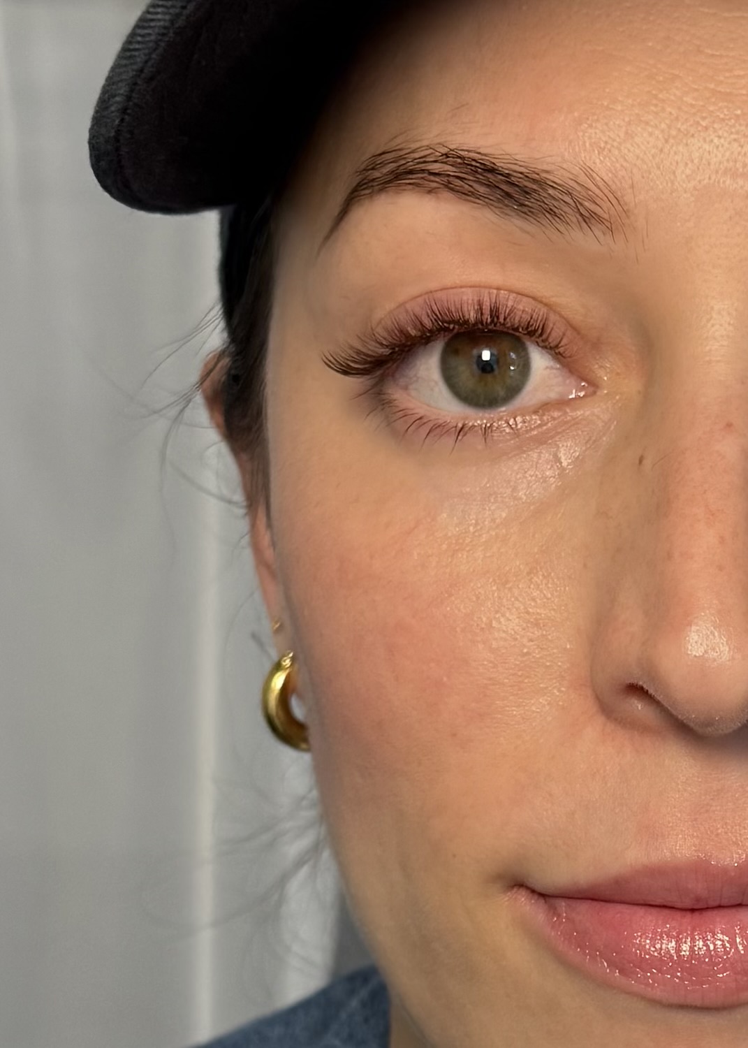Close-up of a woman's face showing her eye, eyebrow, and part of her lips, with a black hat and gold earring visible.