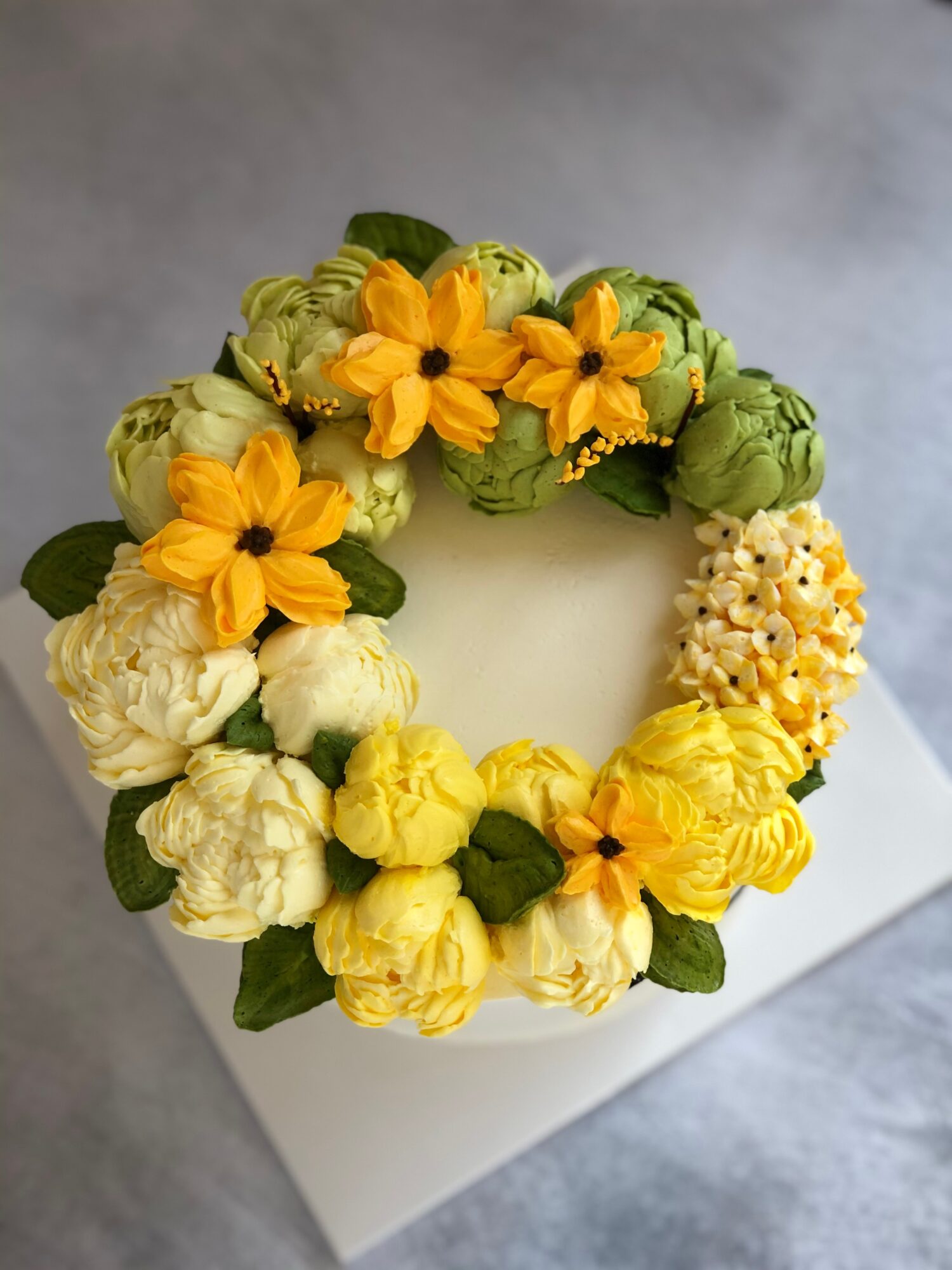 Circular wreath of yellow and white flowers with green leaves on a white board.